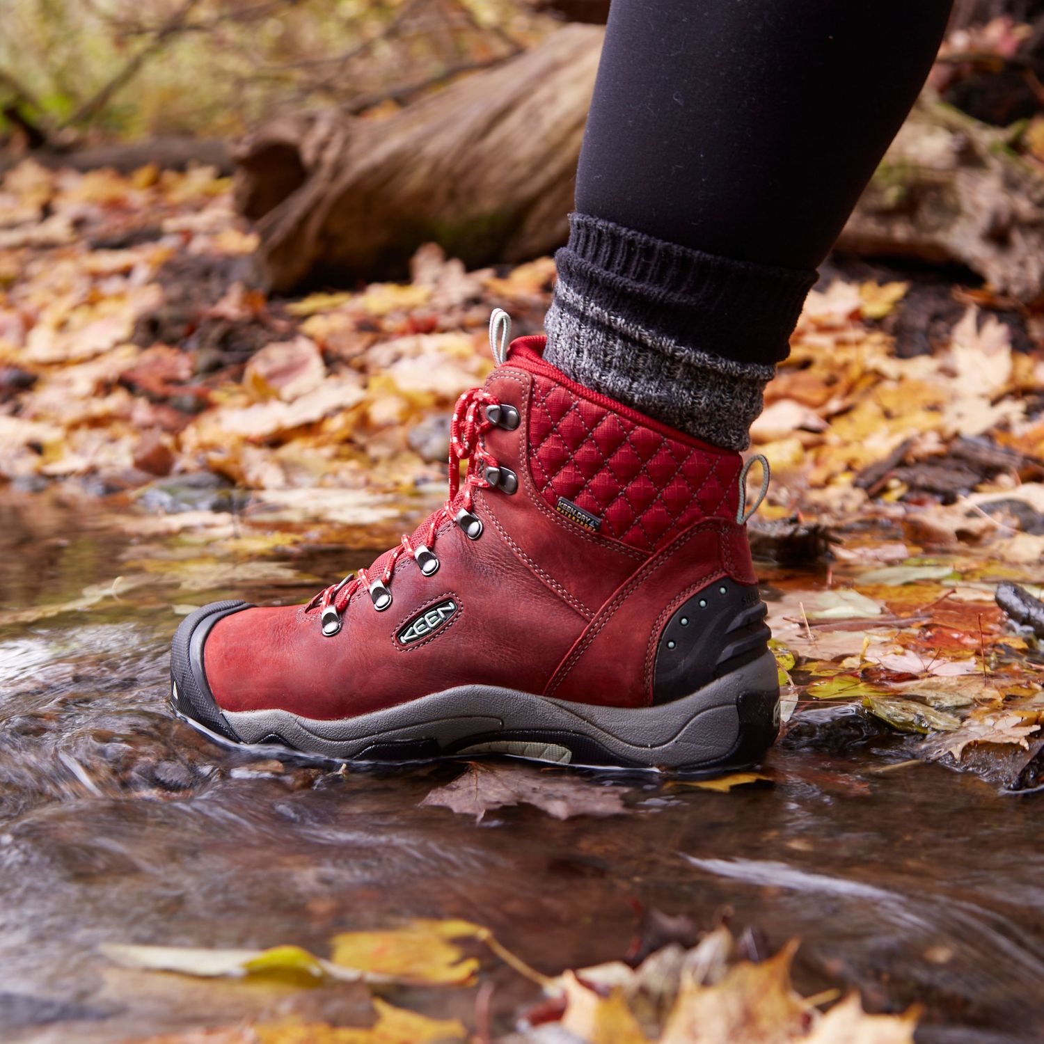 Red hiking boot stepping in autumn leaves and water.