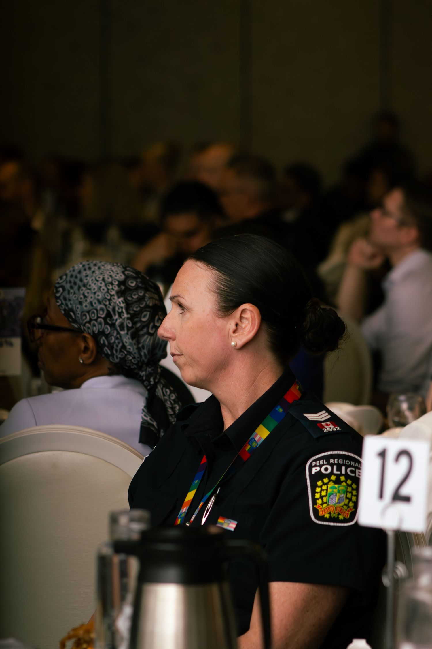 Police officer in uniform sitting at a table during an indoor event with a thermal beverage container visible.