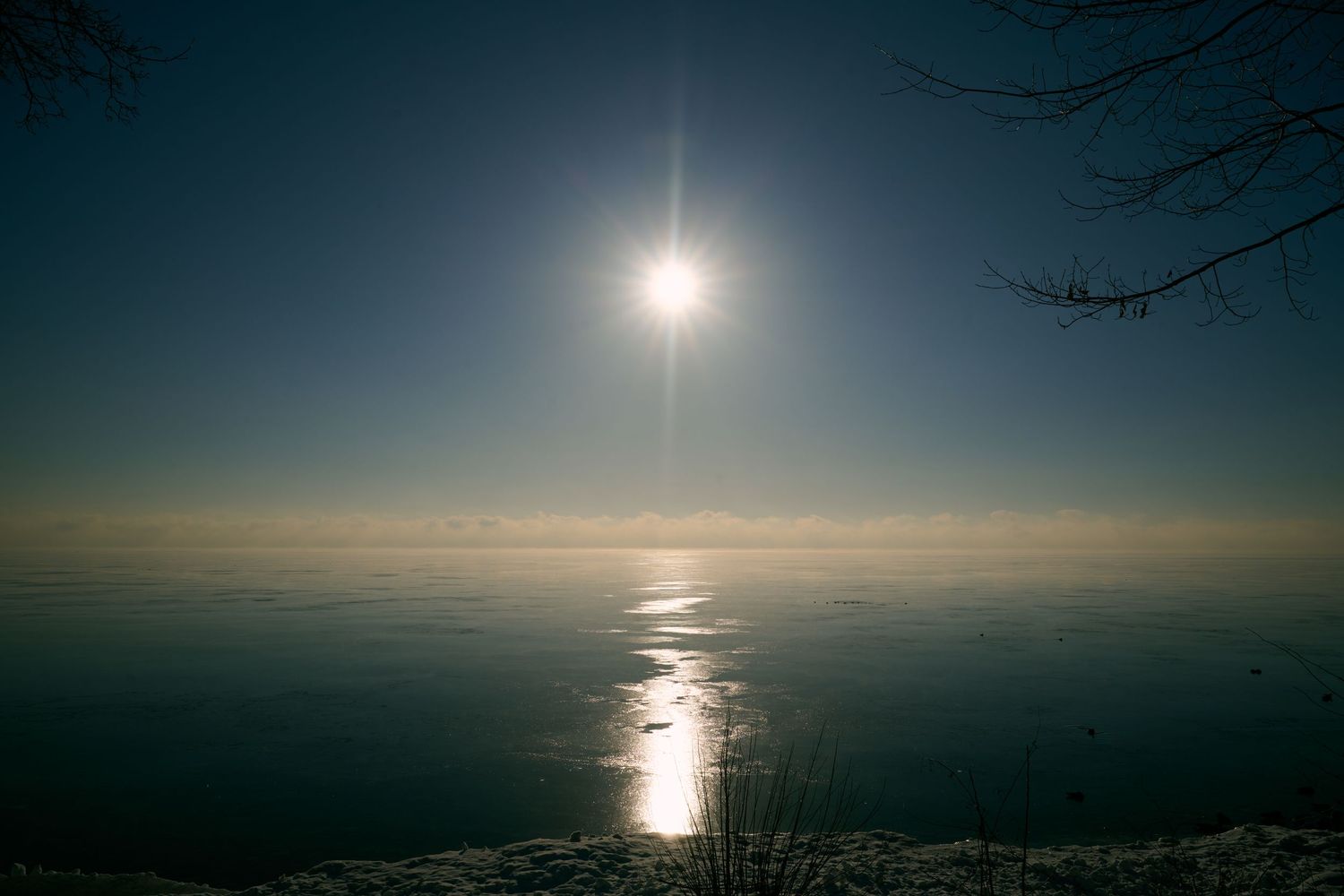 Sun reflects off calm ocean waters at dusk creating a glowing path of light across the dark horizon.