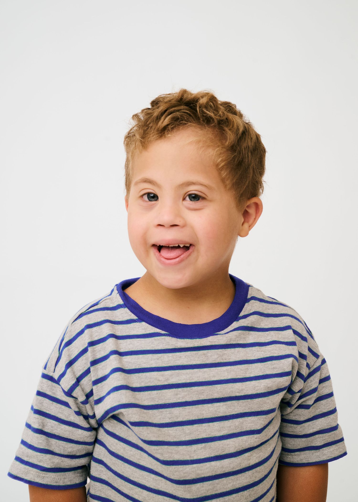 Young child wearing a blue and grey striped shirt smiling against a white background.