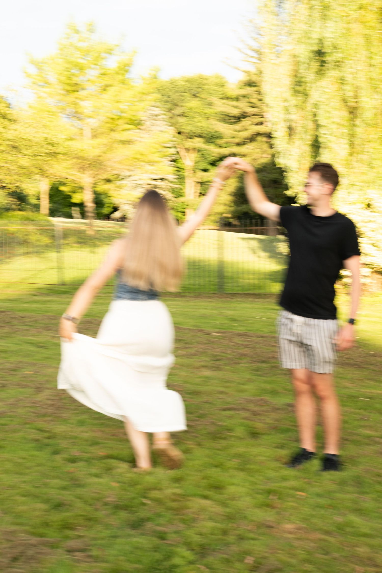 Two people dancing together in a park with sunlit trees creating a dreamy yellow backdrop during golden hour.