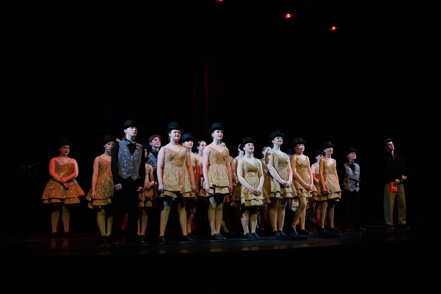 Performers stand in a line on a dark stage during a theatrical performance with dramatic lighting.