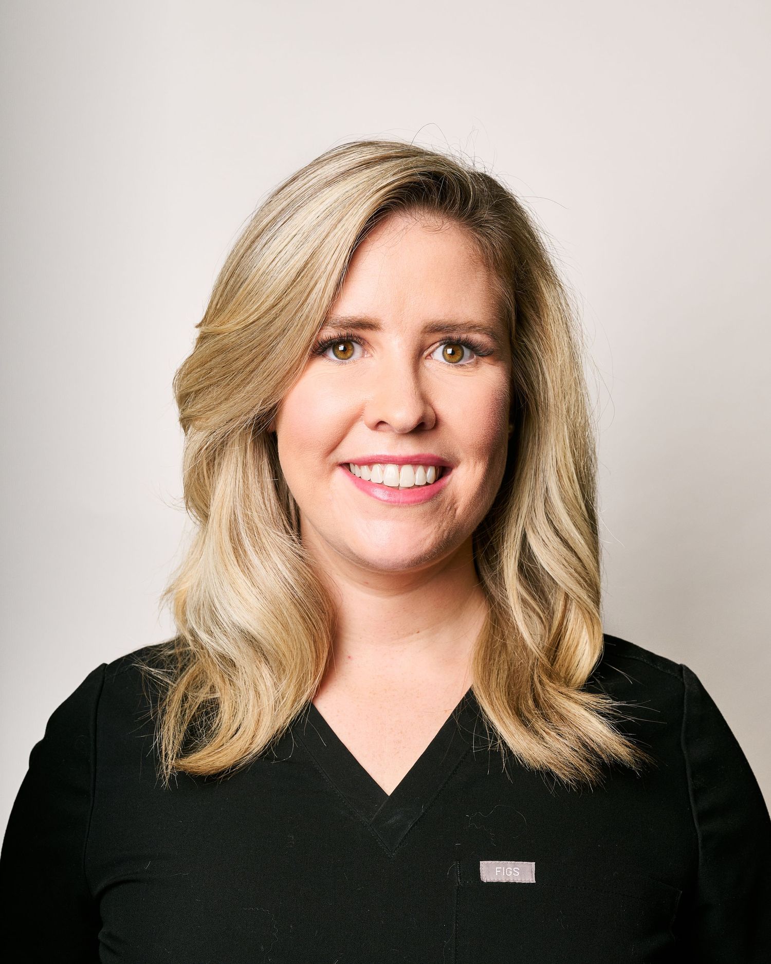 Smiling blonde woman in black medical scrubs poses for a professional healthcare staff portrait photo.