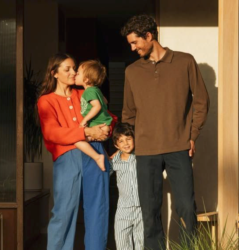 Family in casual attire stands together on a porch during golden hour lighting.