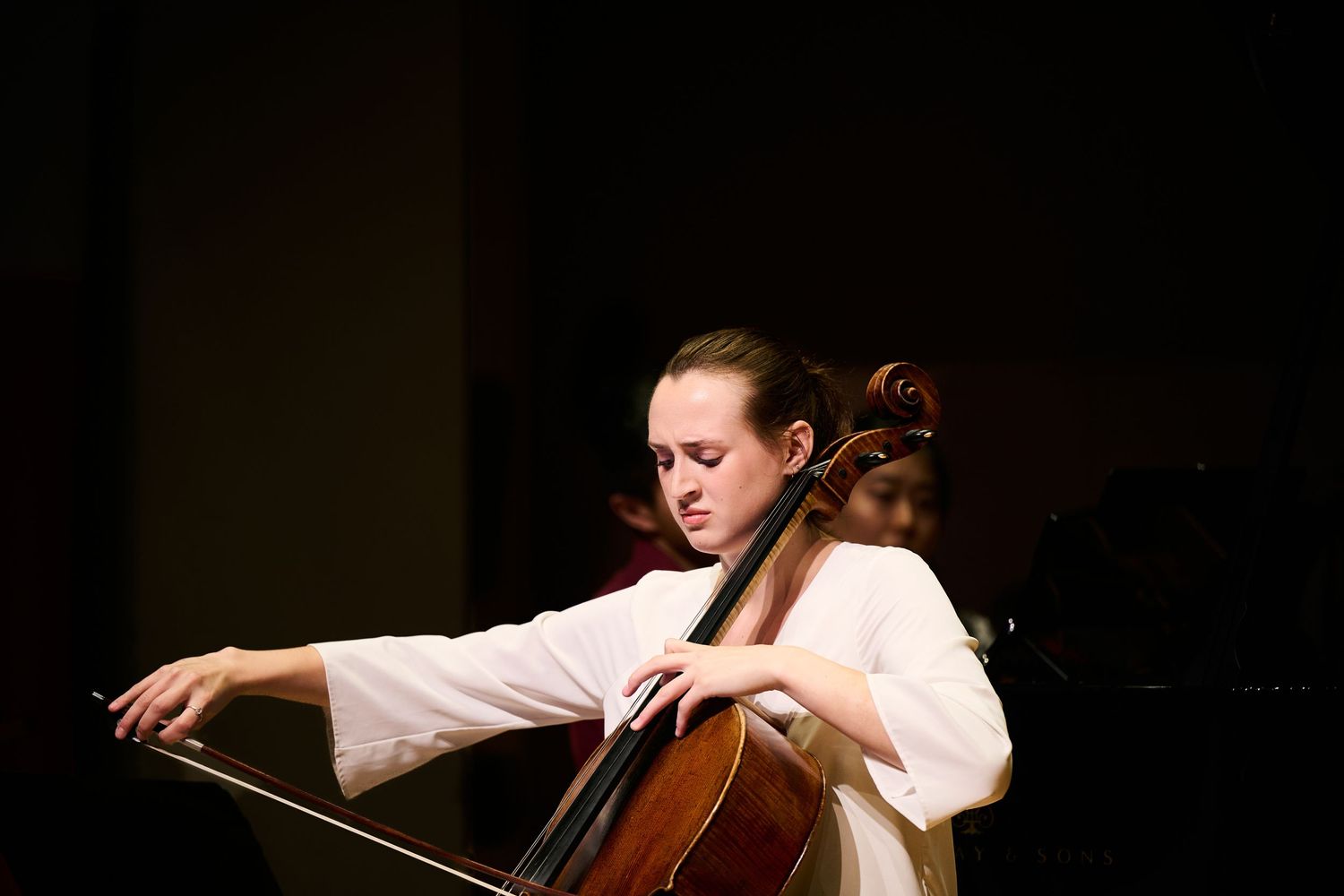 Young woman in white dress playing cello on stage during a classical music performance.