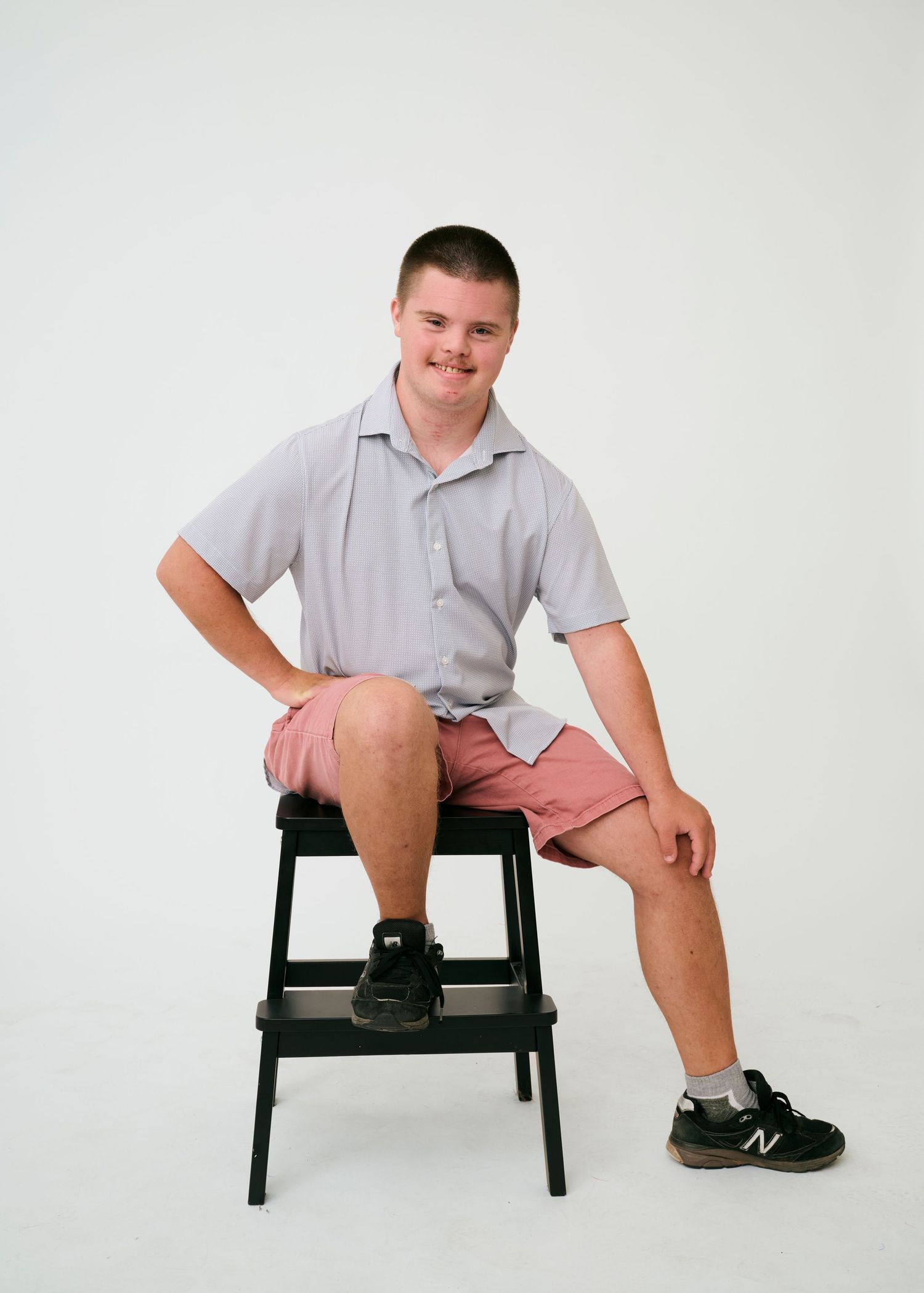 Multiple shots of someone sitting and posing on a black bench against a white backdrop.