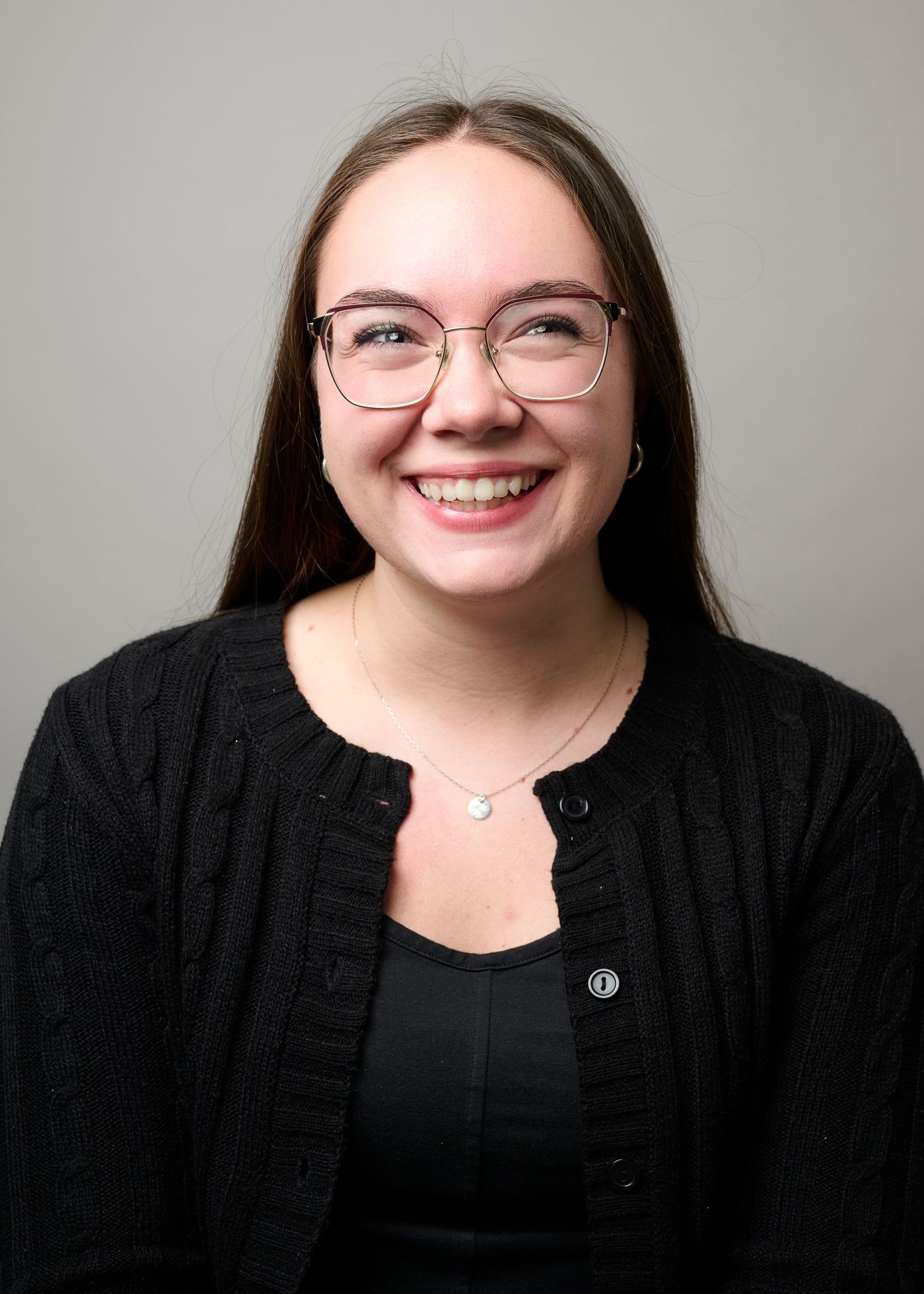 Professional headshot of someone wearing glasses and a black cardigan over dark top, with bright genuine smile against neutral background.