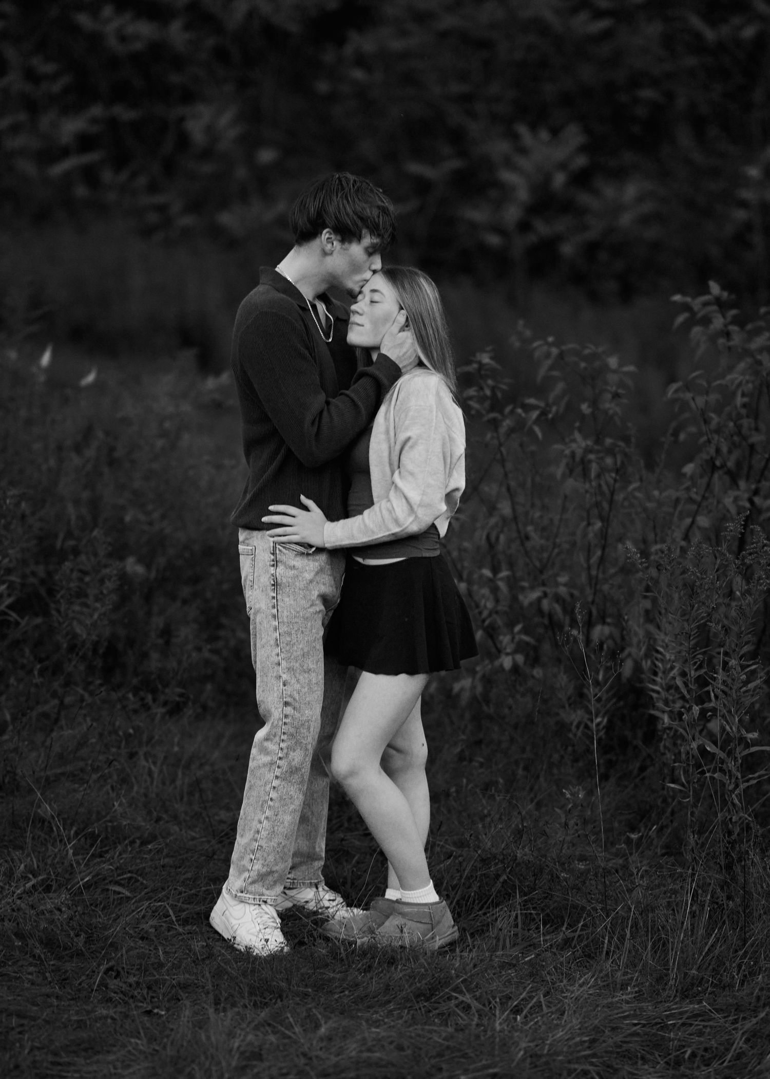 A romantic black and white photo series showing a couple embracing in a field of tall grass at dusk.