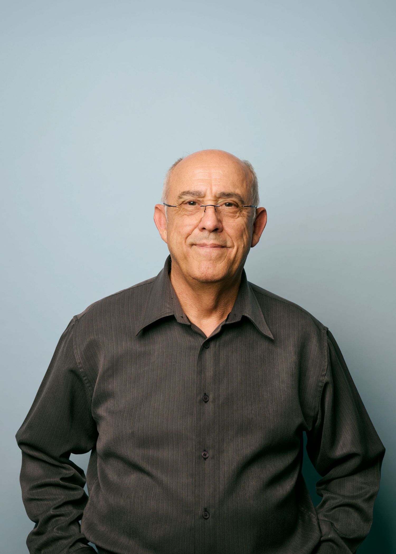 Professional studio portrait of a person in a dark button-down shirt against a light blue background.