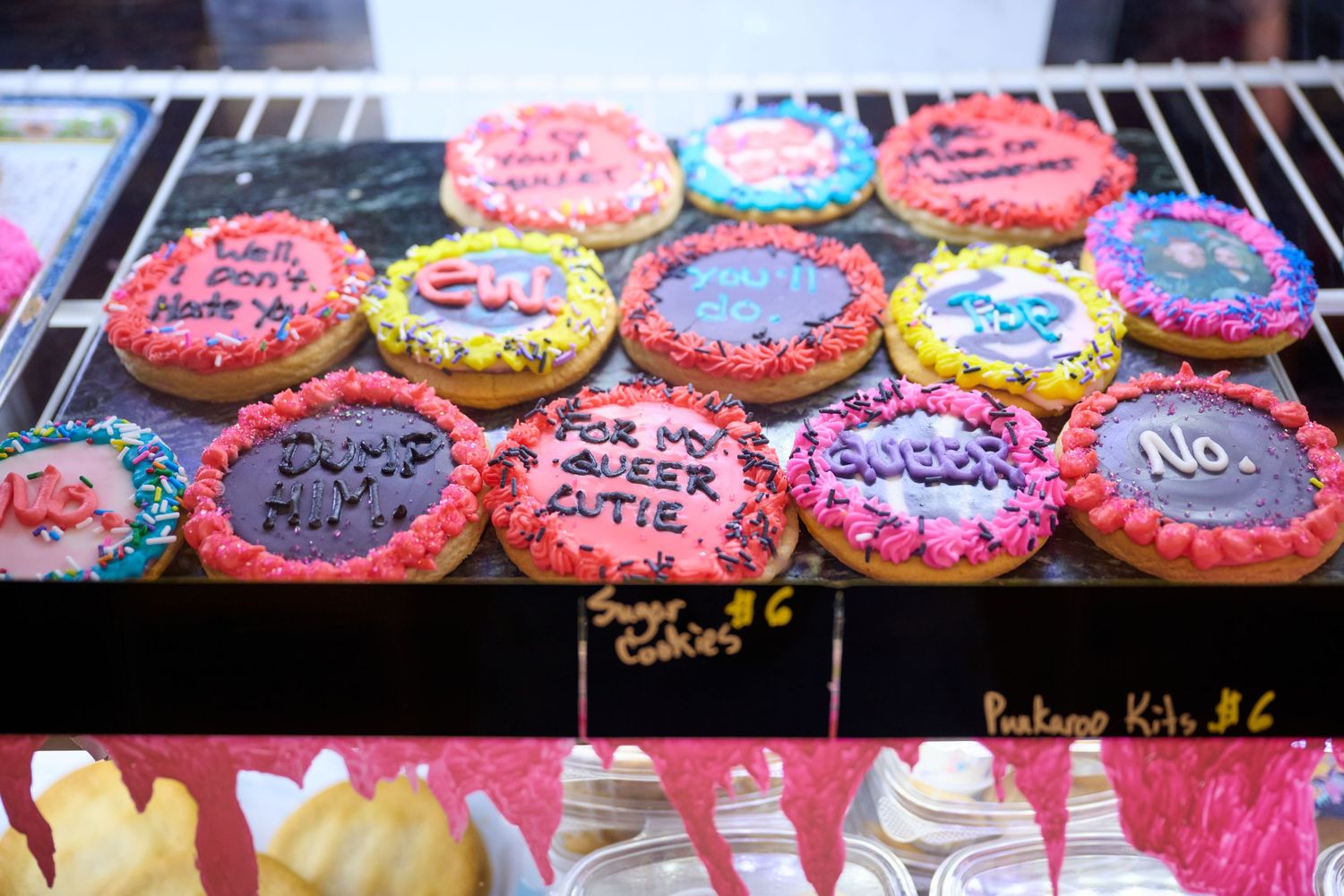 Colorful decorated sugar cookies with pink, blue and purple icing arranged in a bakery display case.