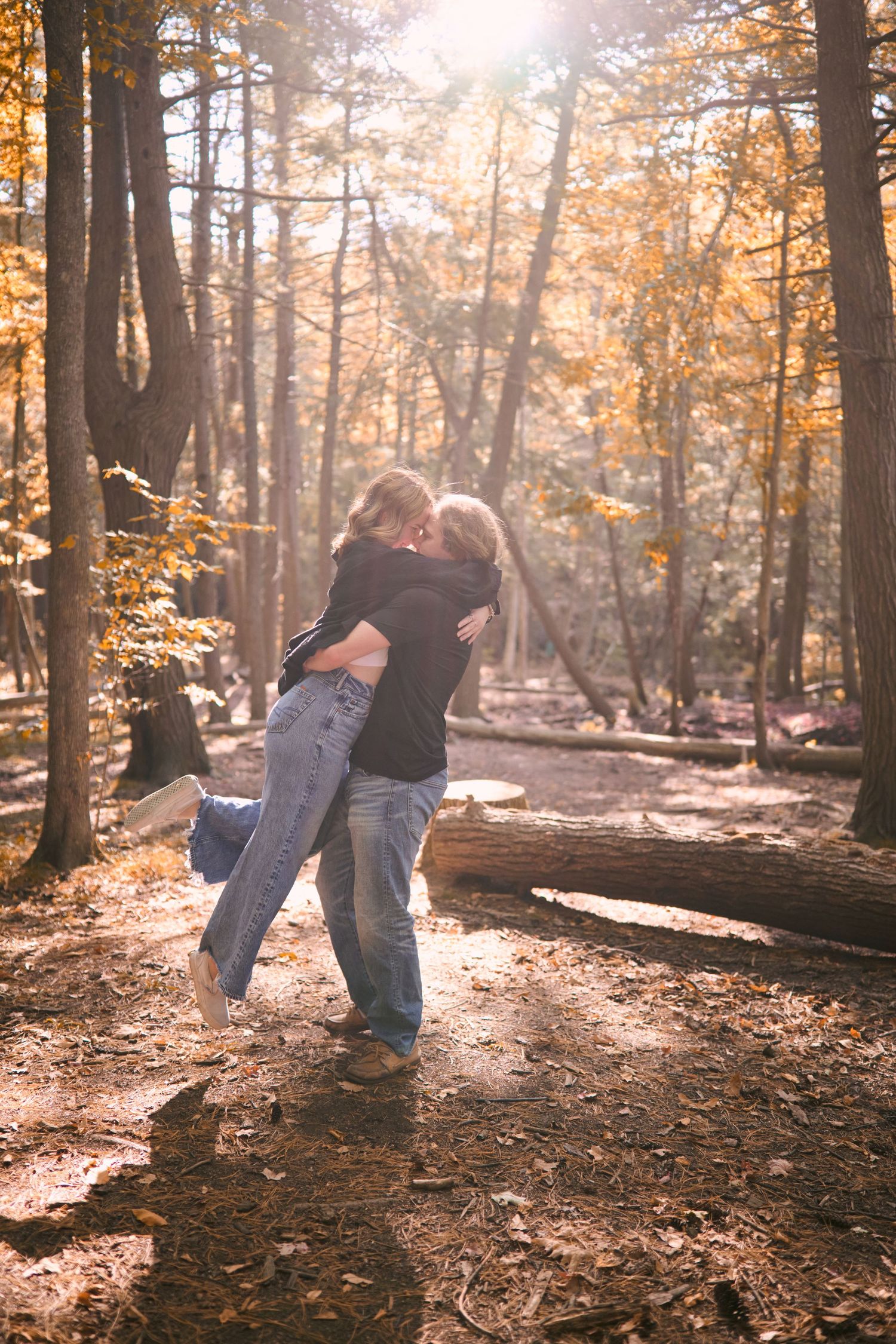 A couple embraces in a sunlit autumn forest with golden leaves and streaming sunbeams through the trees.