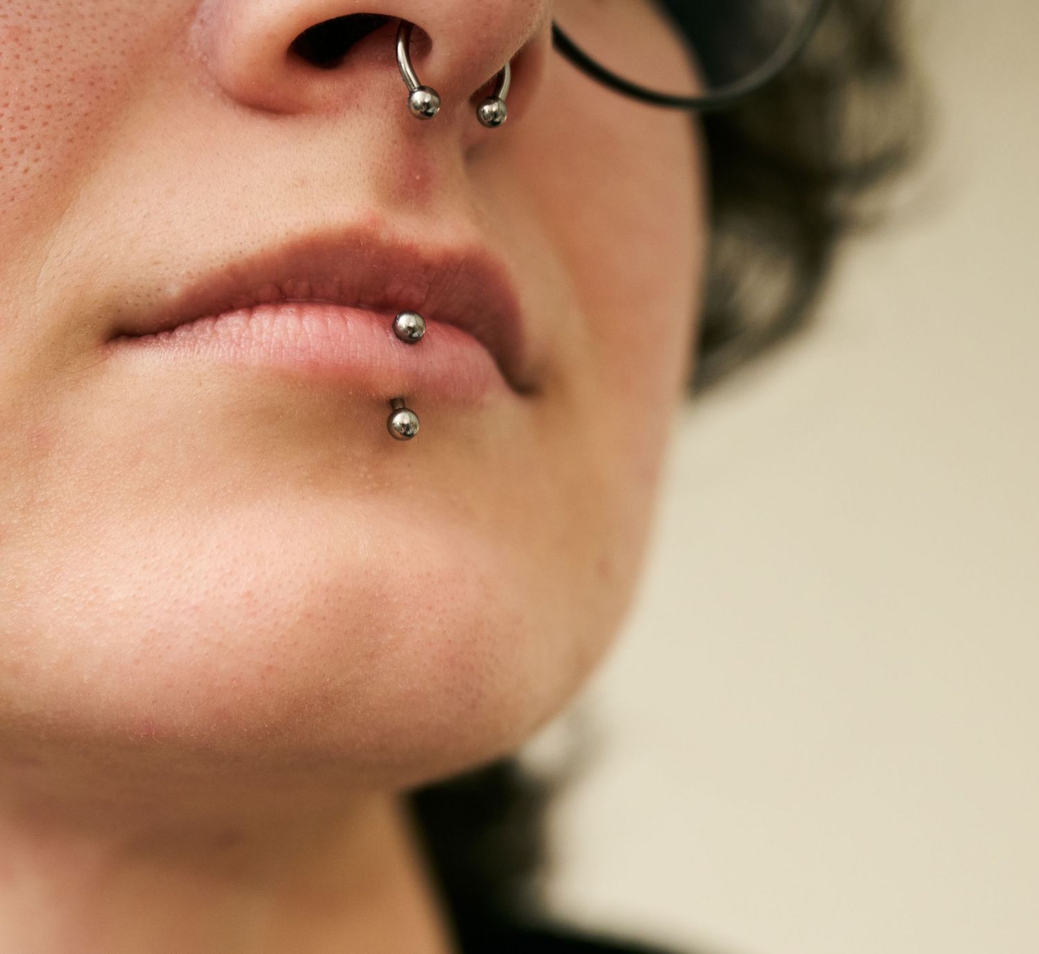 Close-up view of facial piercings including septum and lip jewelry against a blurred background.