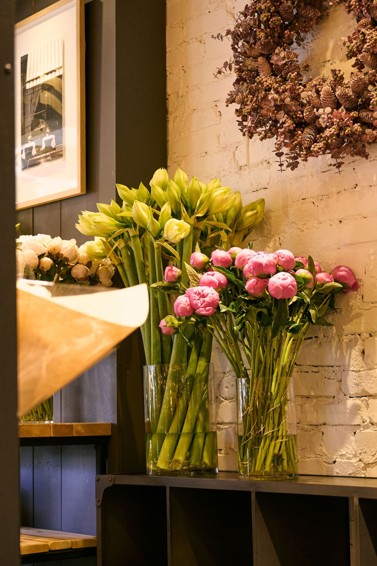 Fresh pink ranunculus and yellow tulip flowers arranged in glass vases against an exposed brick wall with rustic decor.