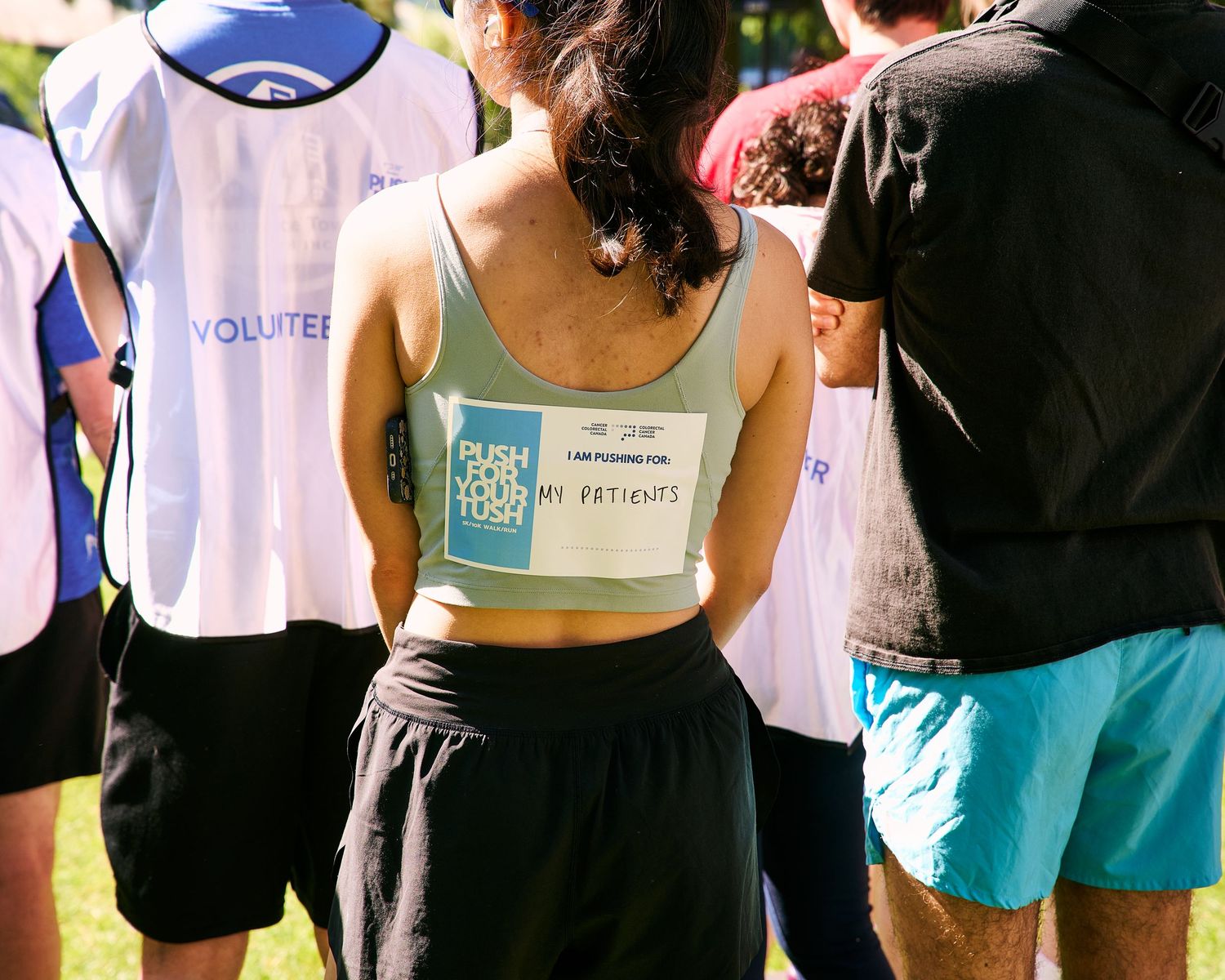 Runner wearing a tank top with motivational text at an outdoor charity race event surrounded by volunteers.