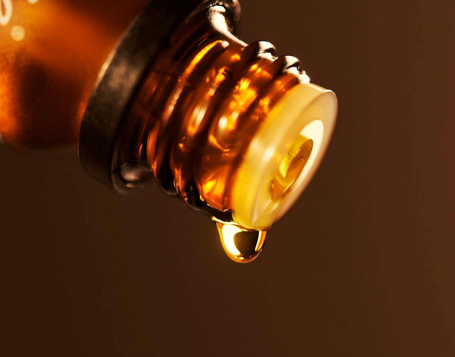 Amber liquid dropping from a glass bottle neck in macro photography.