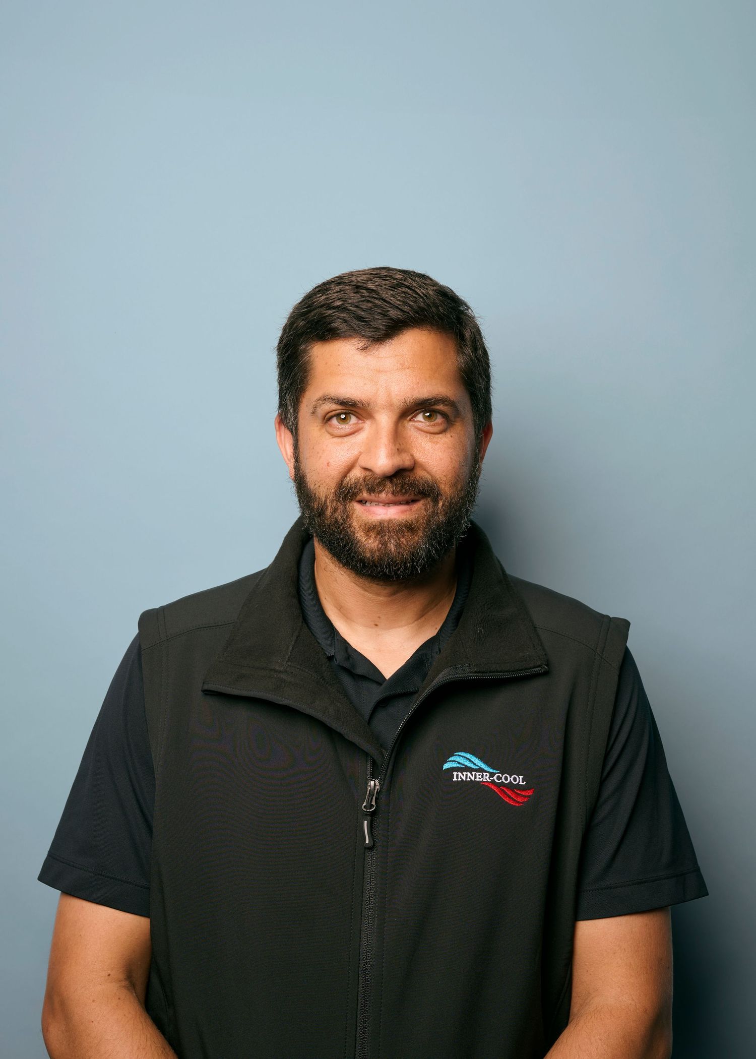 Professional headshots against a gray background showing a person in a black polo shirt with a company logo.