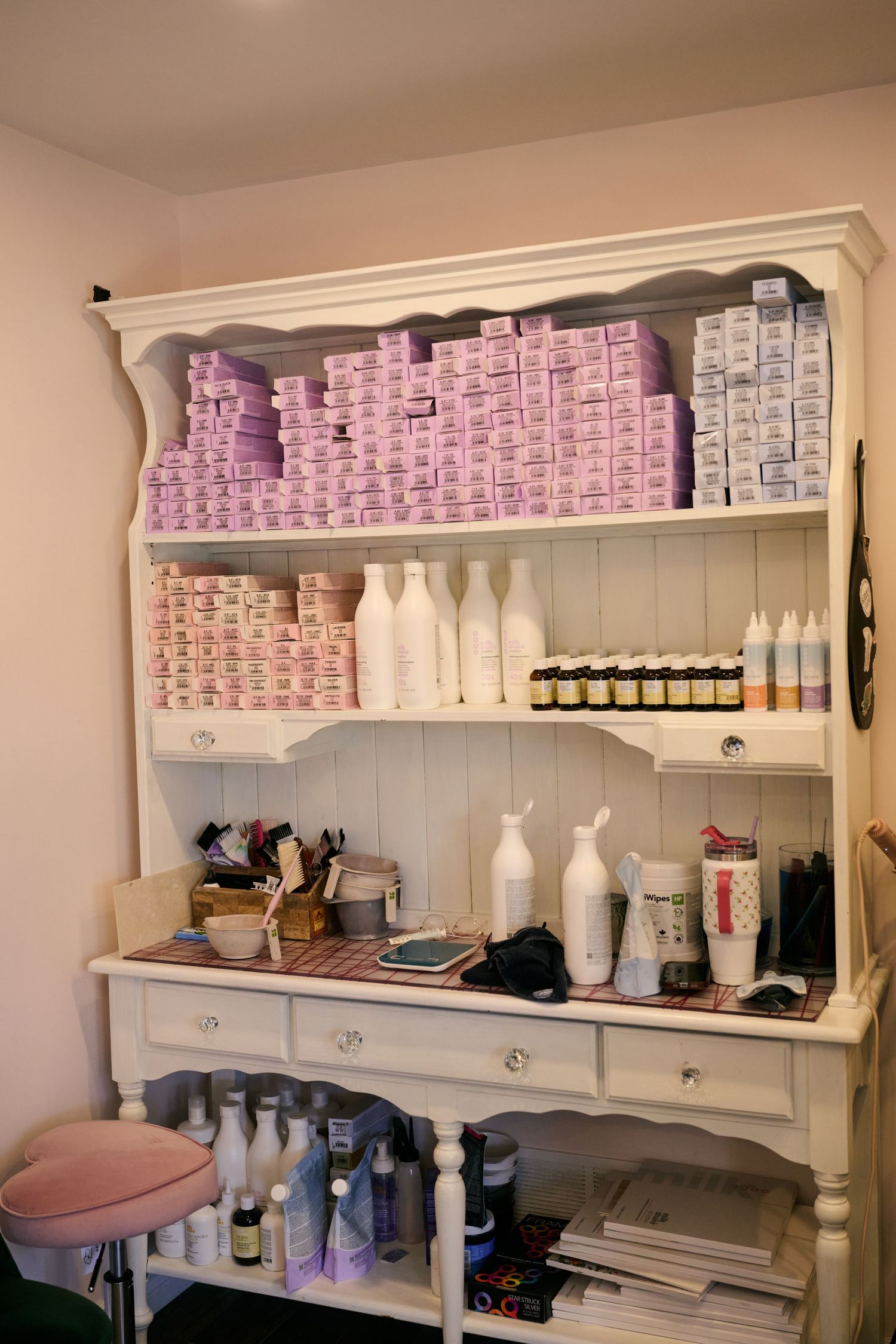 Vintage white display shelf stocked with beauty salon supplies including pink and white product boxes and styling tools.