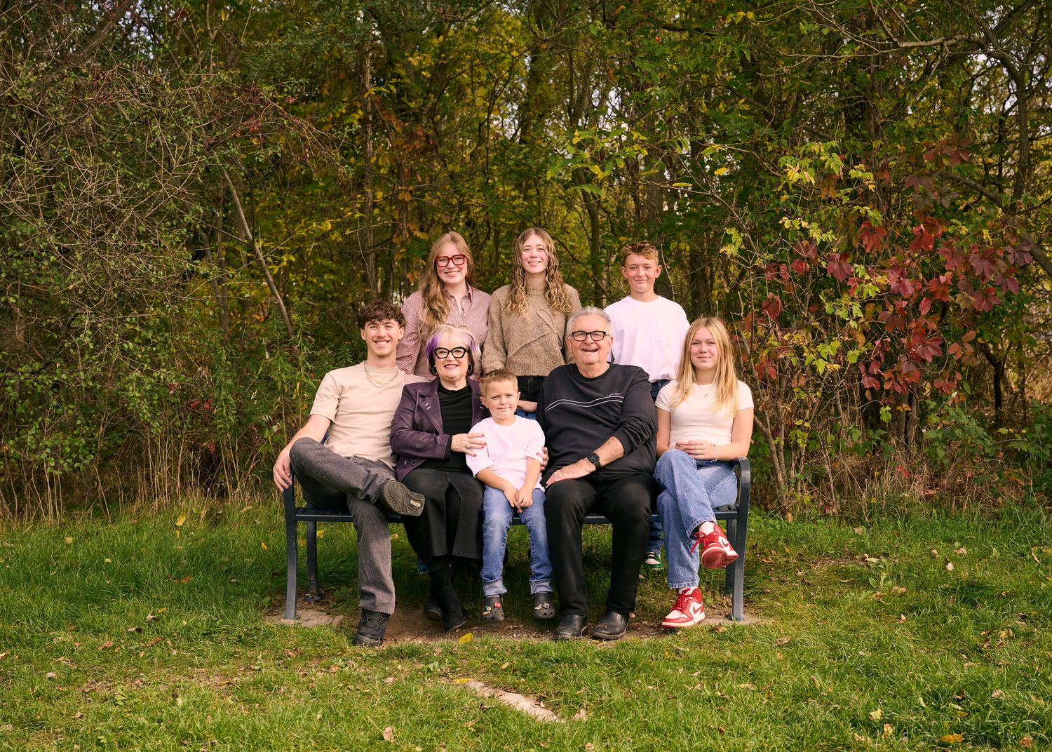 A family portrait series in a natural outdoor setting with trees and grass showing different casual poses.