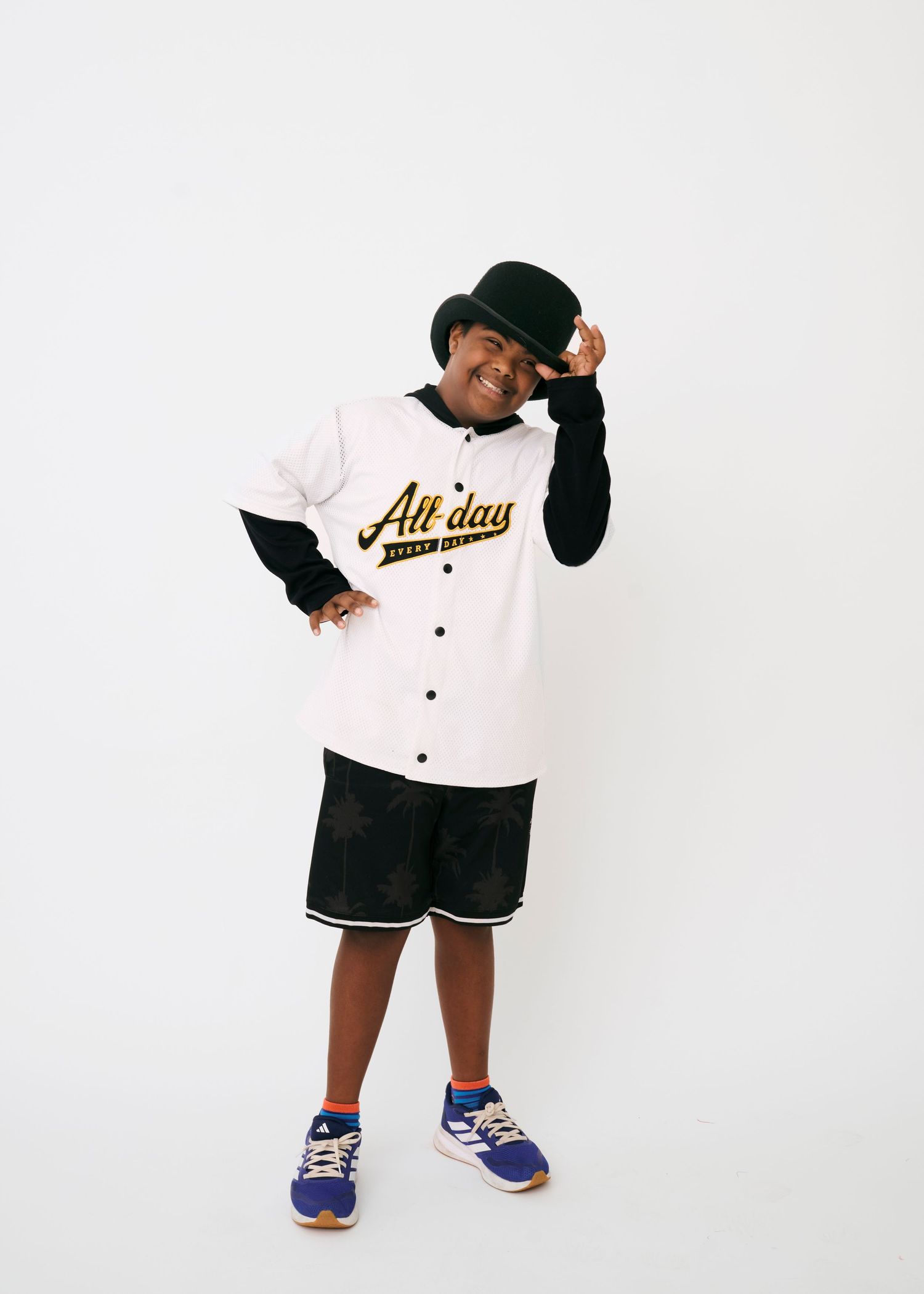Person in black and white baseball uniform and cap poses in four different playful stances with blue sneakers.