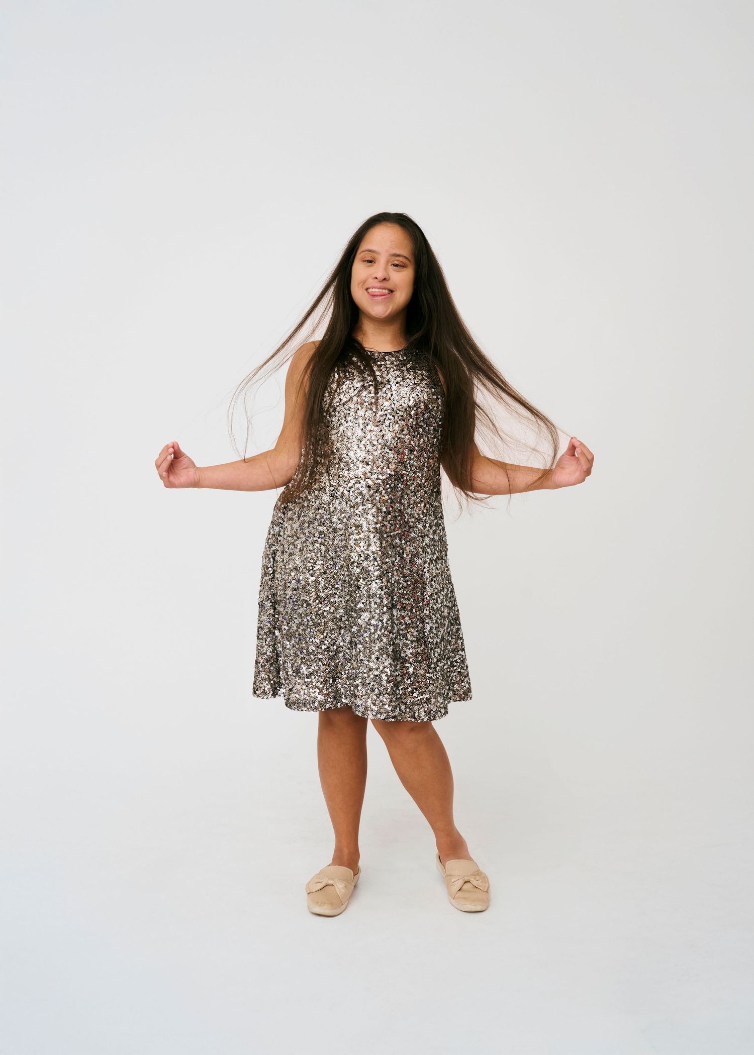 A shimmering sequin dress twirls in motion against a white studio backdrop, paired with soft ballet flats.