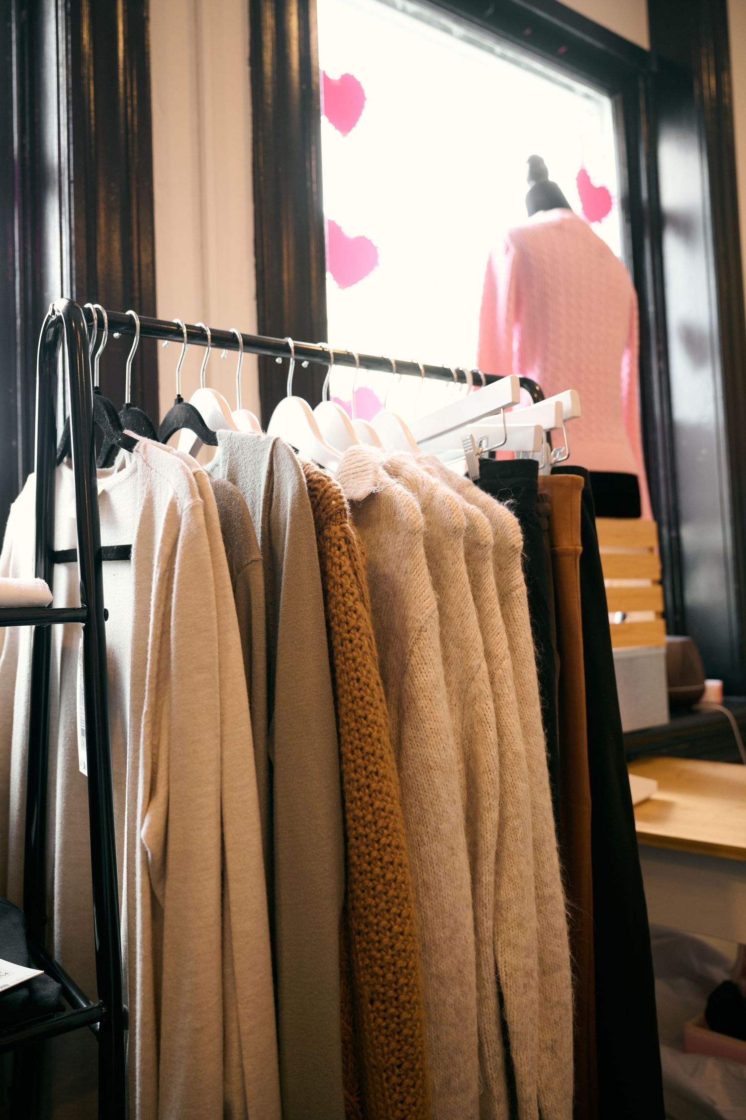 Clothing rack displays neutral-colored sweaters and coats in warm beige and brown tones inside a retail store.
