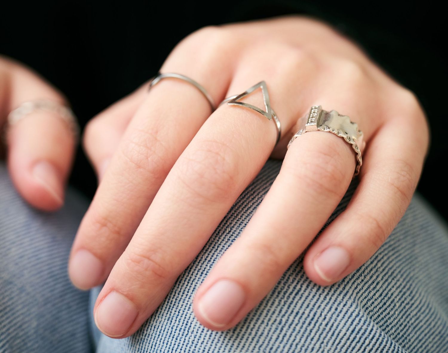 Close-up shot of two minimalist silver rings worn on a hand resting against grey fabric.
