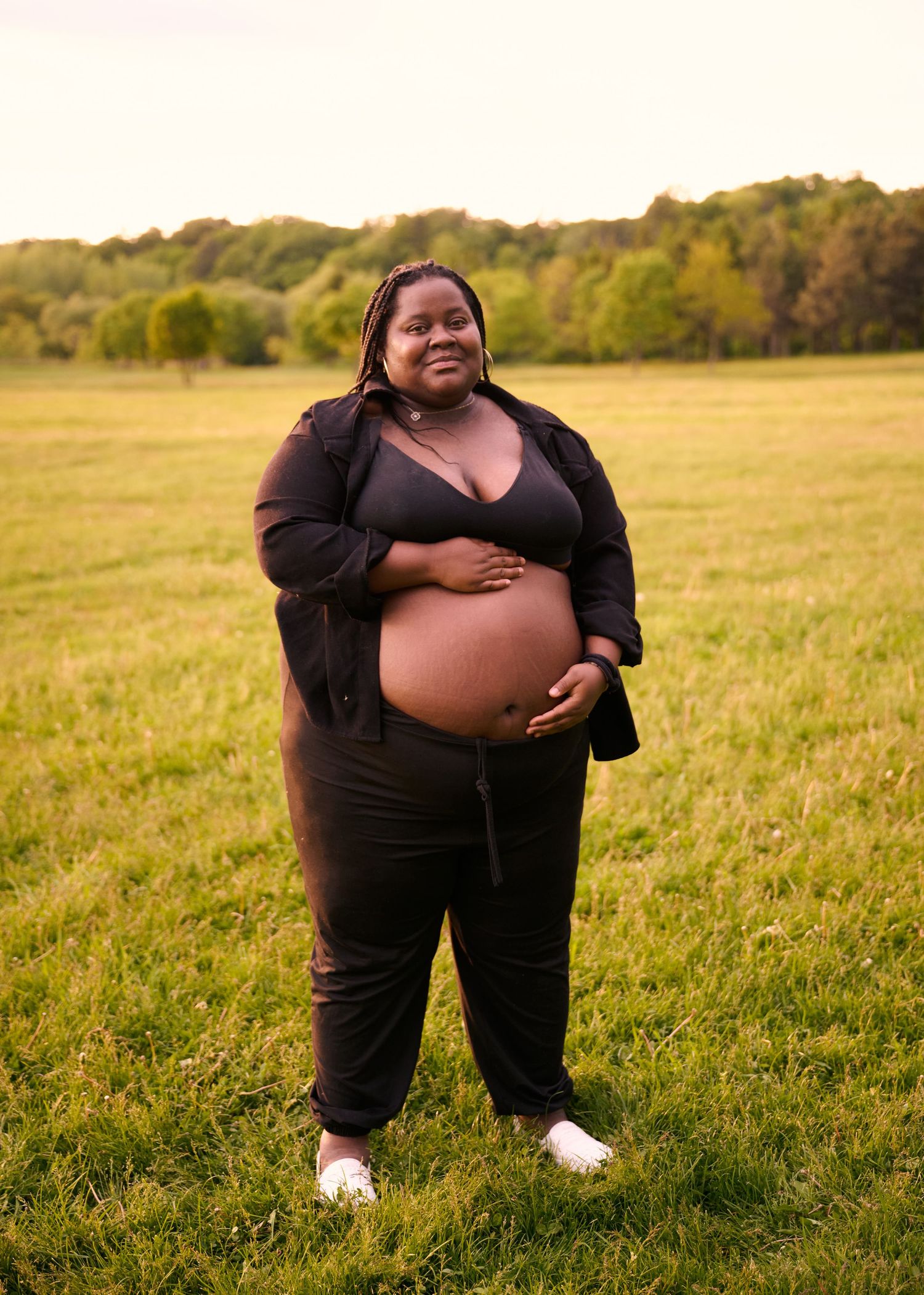 A person wearing a black outfit stands in a sunlit grassy field during golden hour.