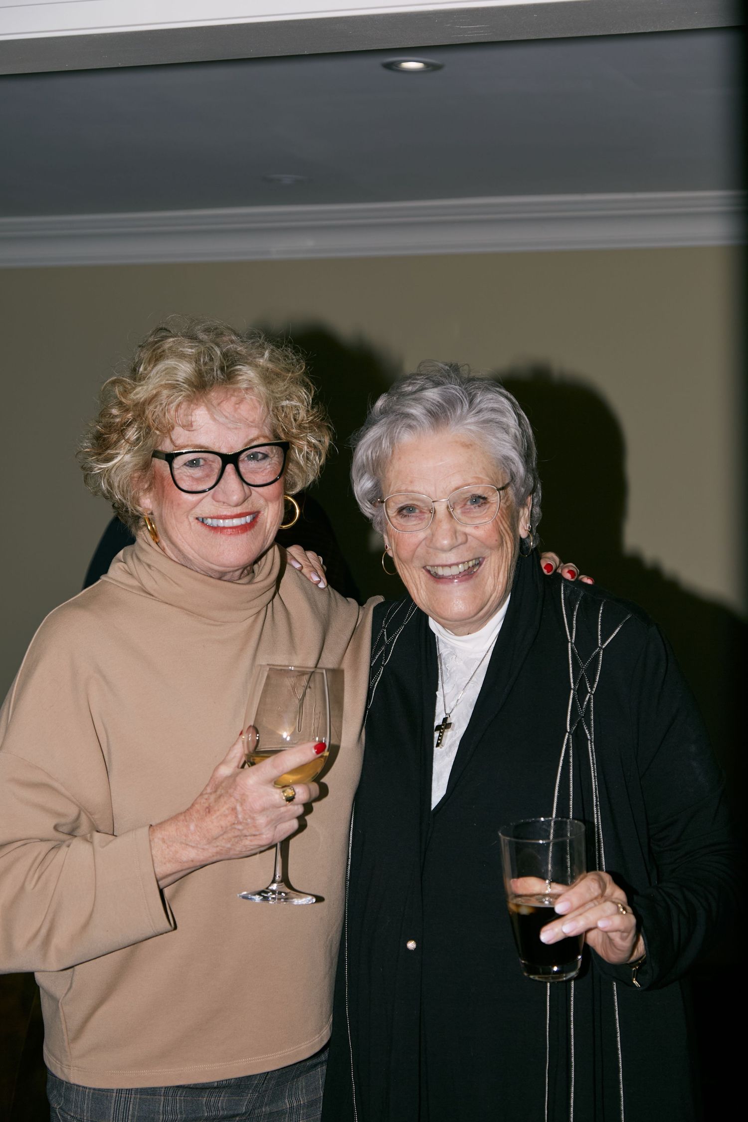 Two people in contrasting outfits share drinks and laughter at a social gathering.