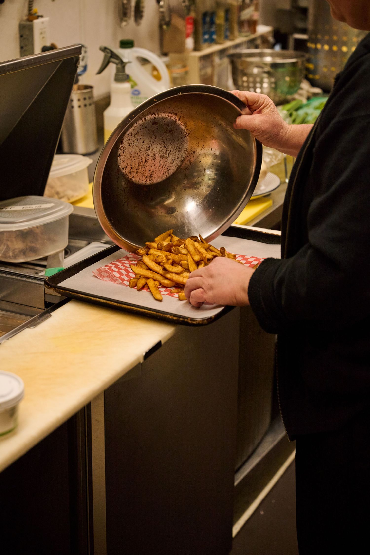 Chef preparing french fries in a commercial kitchen with a metal pan and red lined tray.