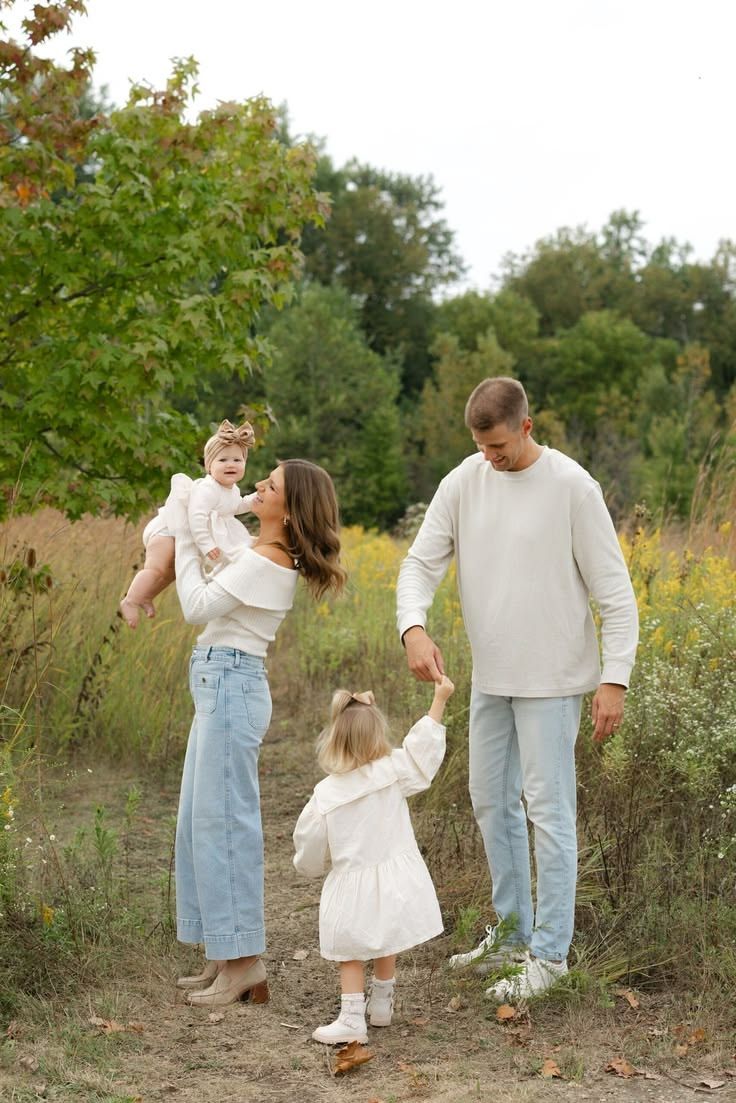 Family of four walking on a nature path, parents holding children, wearing casual white and denim outfits.