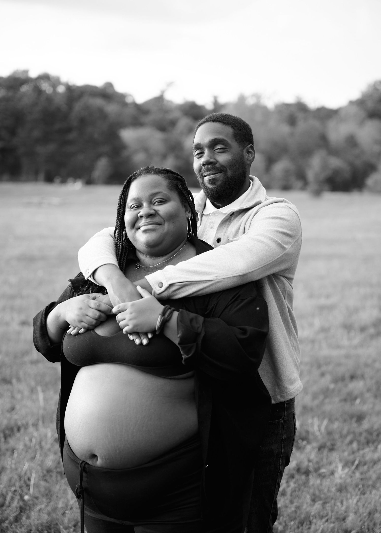 A series of black and white maternity photos showing a couple embracing in a grassy outdoor setting.