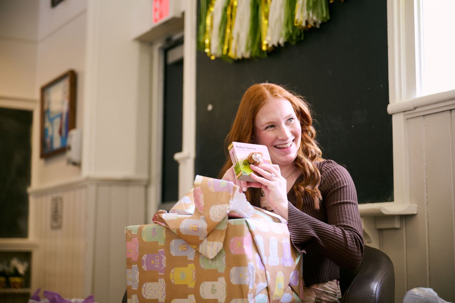 A person in a brown sweater sits at a table with coffee cups and decorative party streamers hanging overhead.