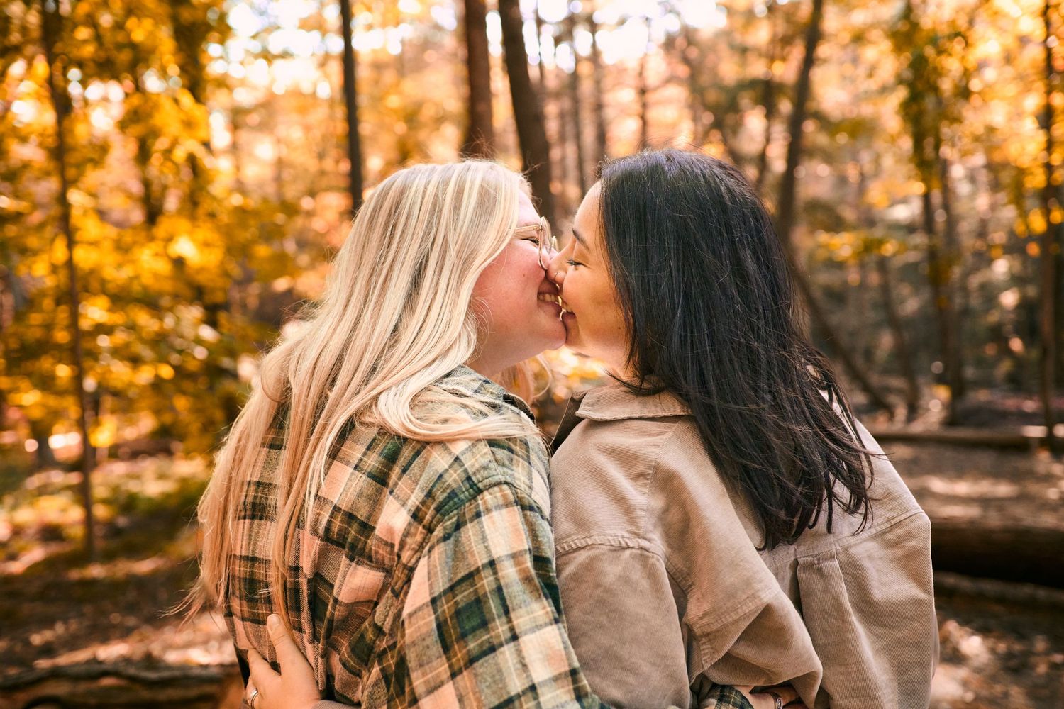 Two people sit together outdoors during golden hour as autumn leaves glow in warm sunlight behind them.