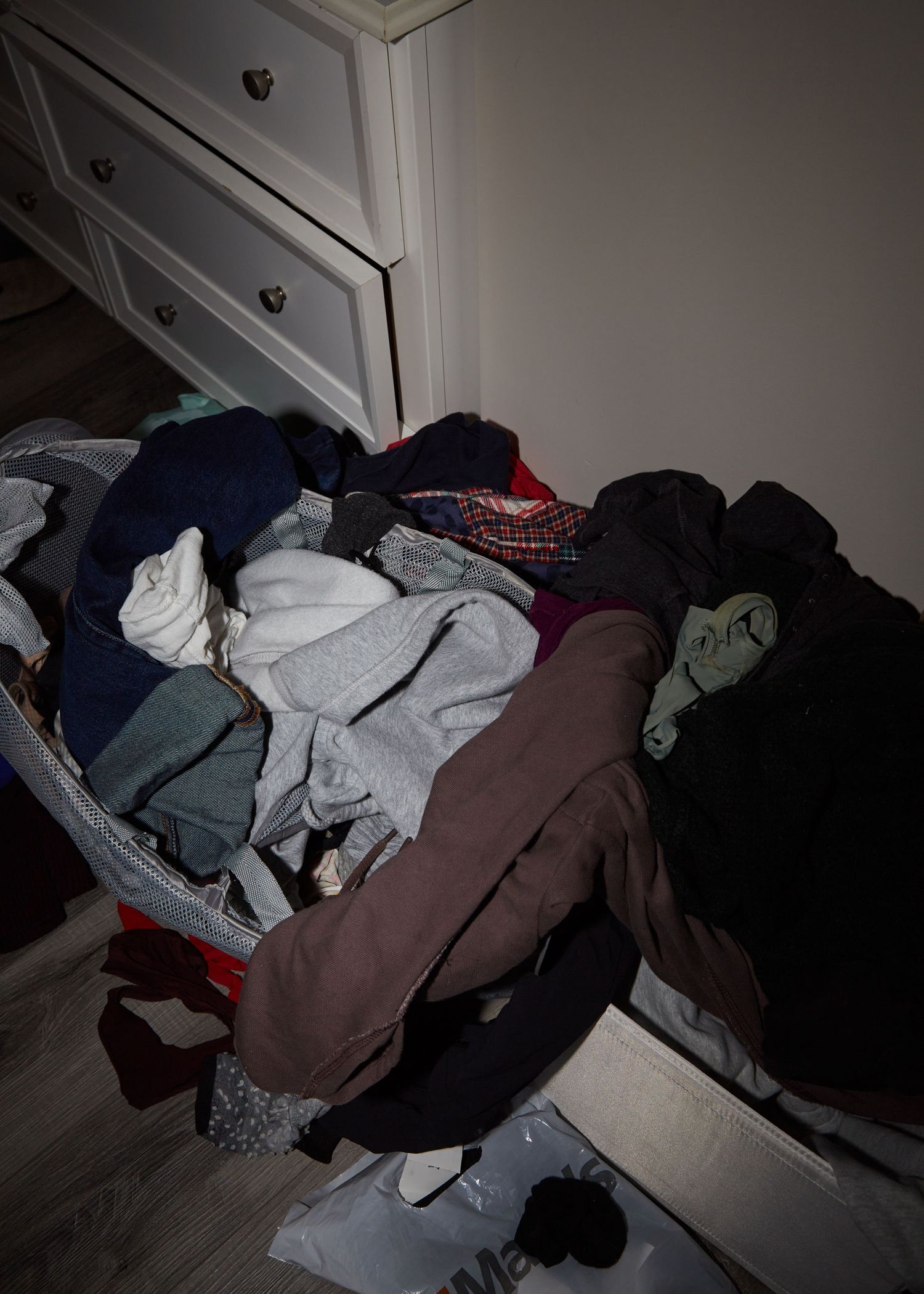 A messy pile of clothes and laundry near a white dresser with drawers.