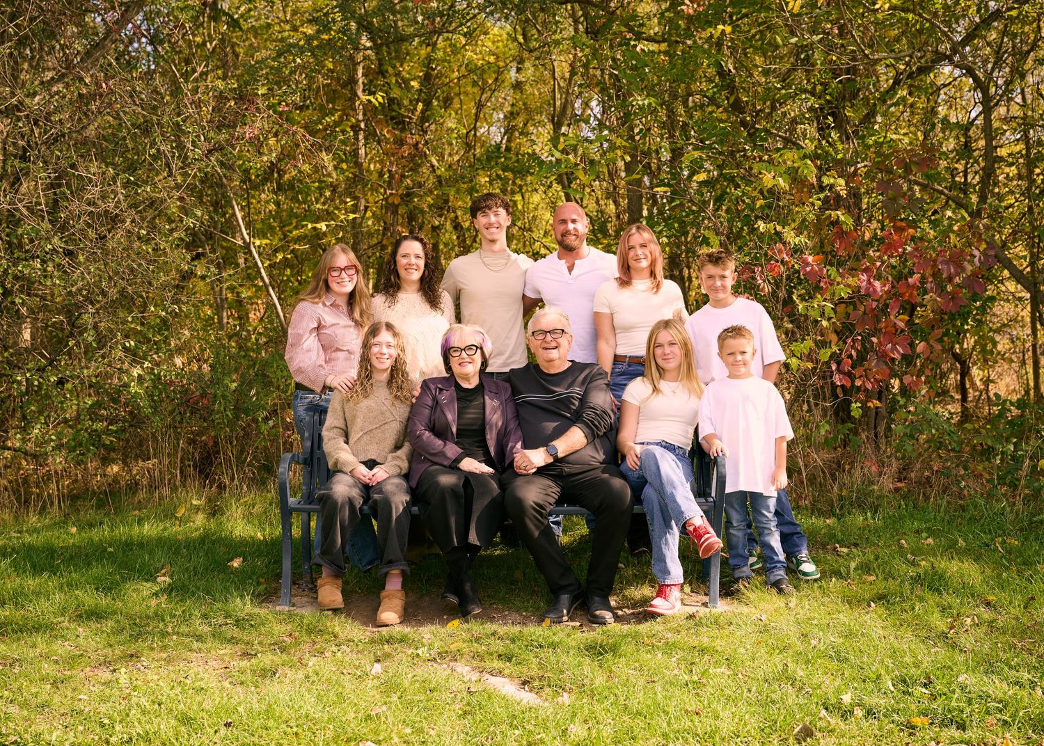 Large family group portrait outdoors in autumn garden with green and red foliage background.