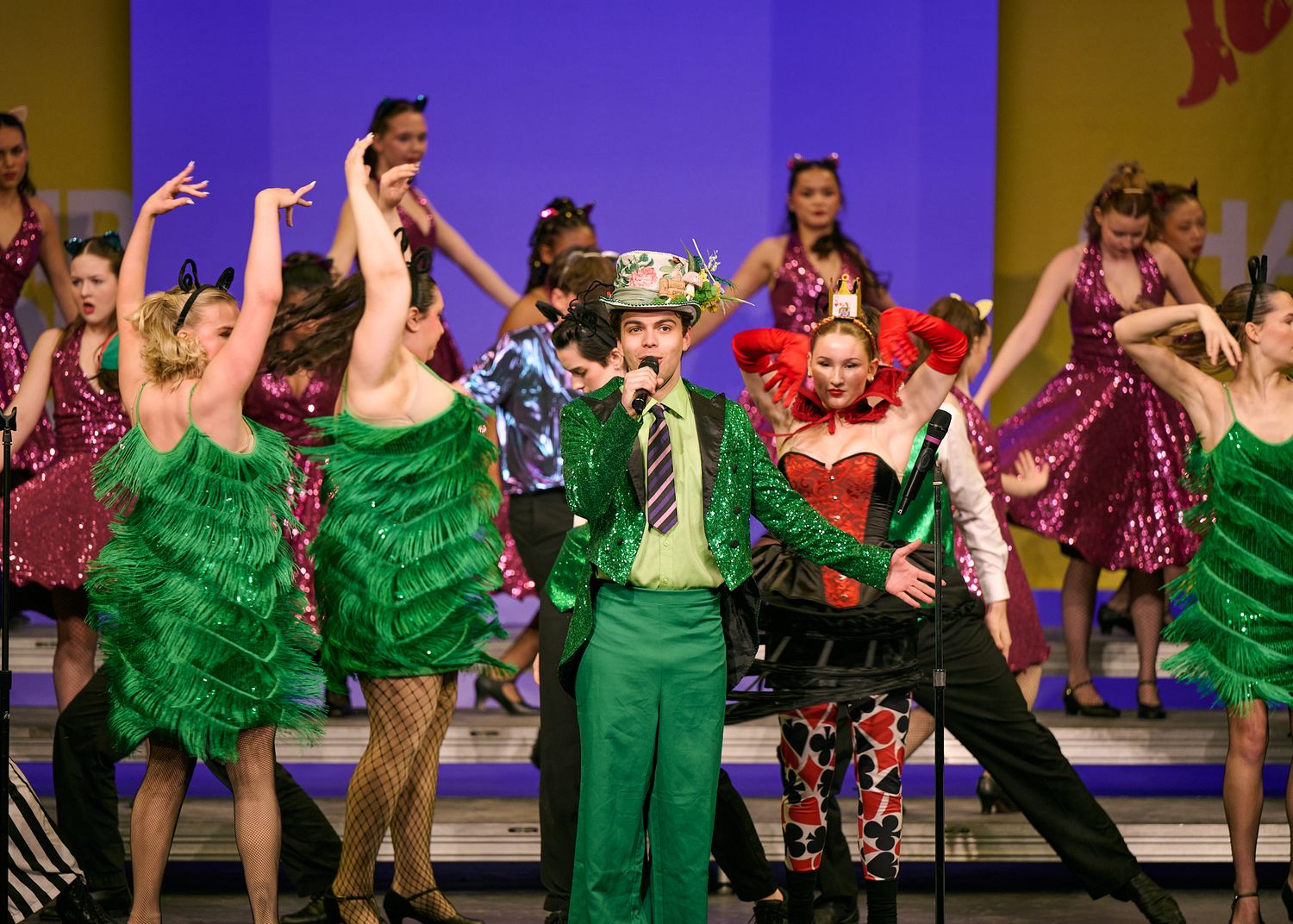 Performers in colorful costumes dancing on stage during a theatrical musical production.