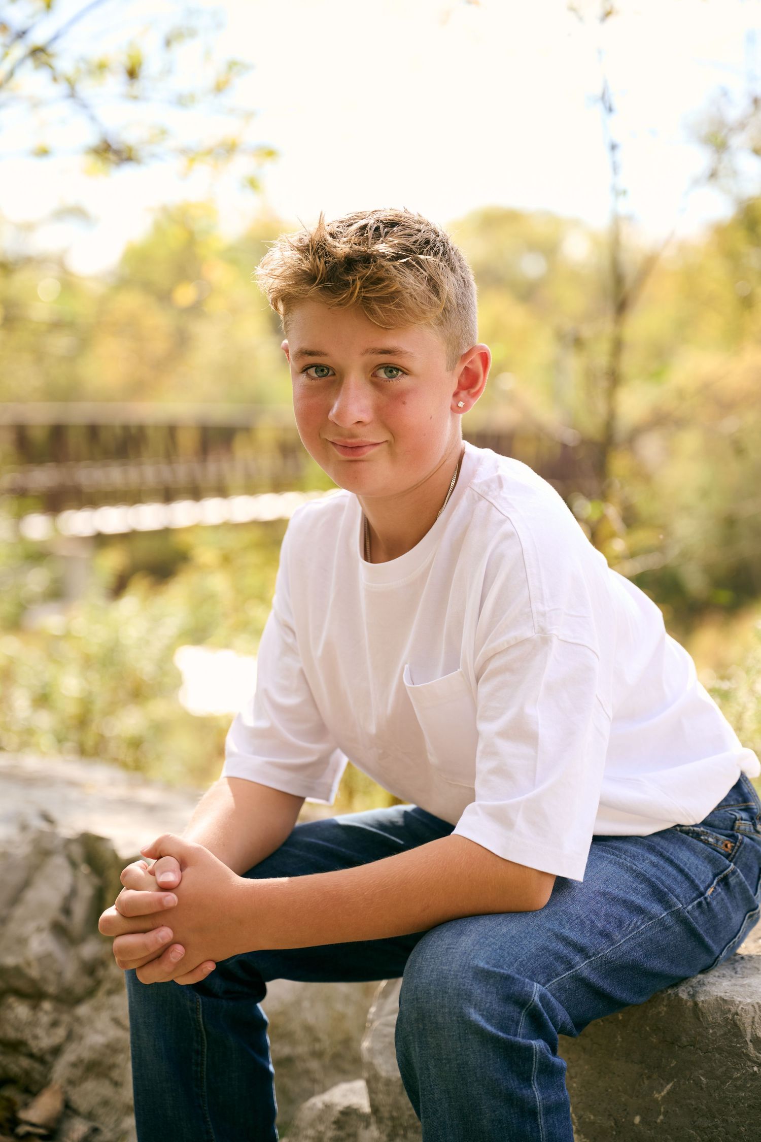 A young person in a white t-shirt and jeans sits casually on rocks outdoors in warm natural lighting.