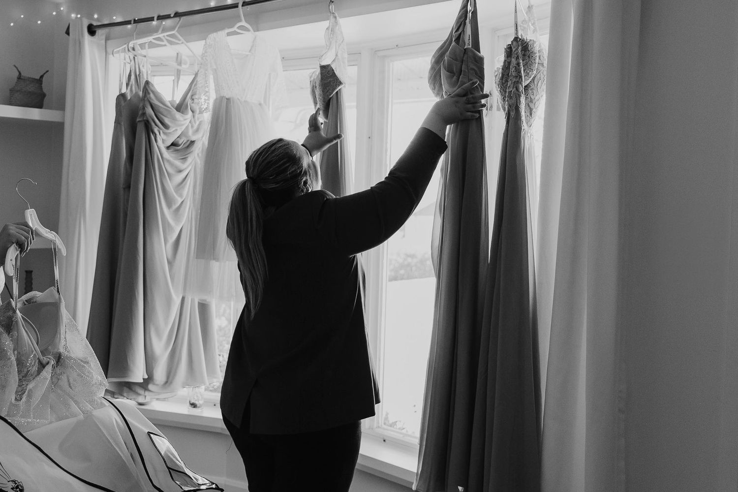 A silhouetted figure reaches up to arrange dresses on display in what appears to be a clothing store or boutique.