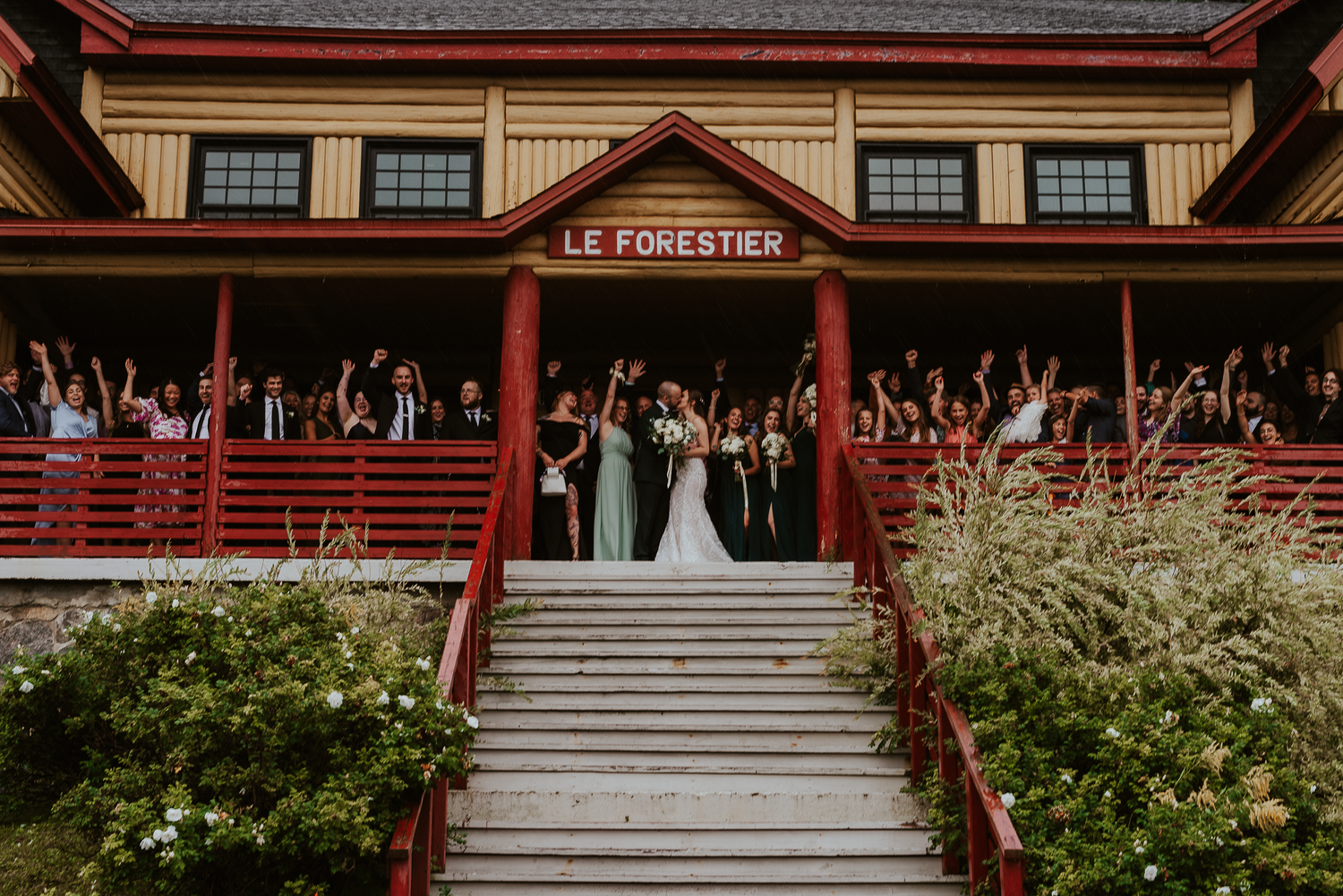 Wedding party poses on steps of Le Forestier venue with red exterior.