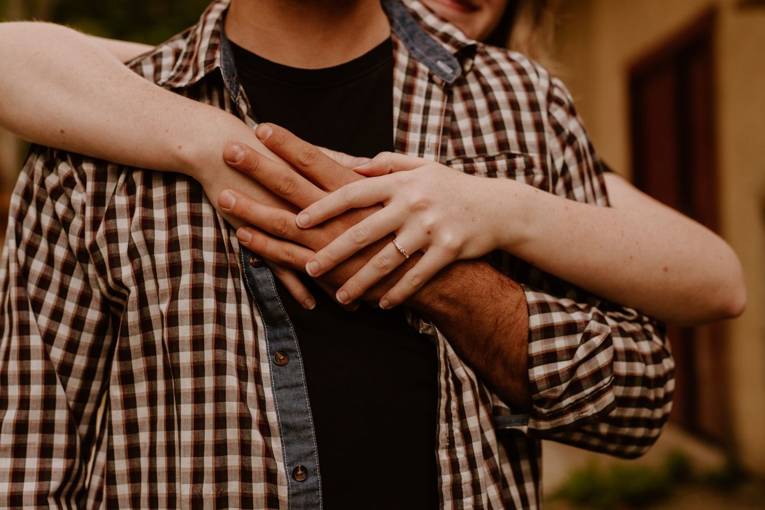 Close up of hands embracing showing engagement ring against plaid shirt.