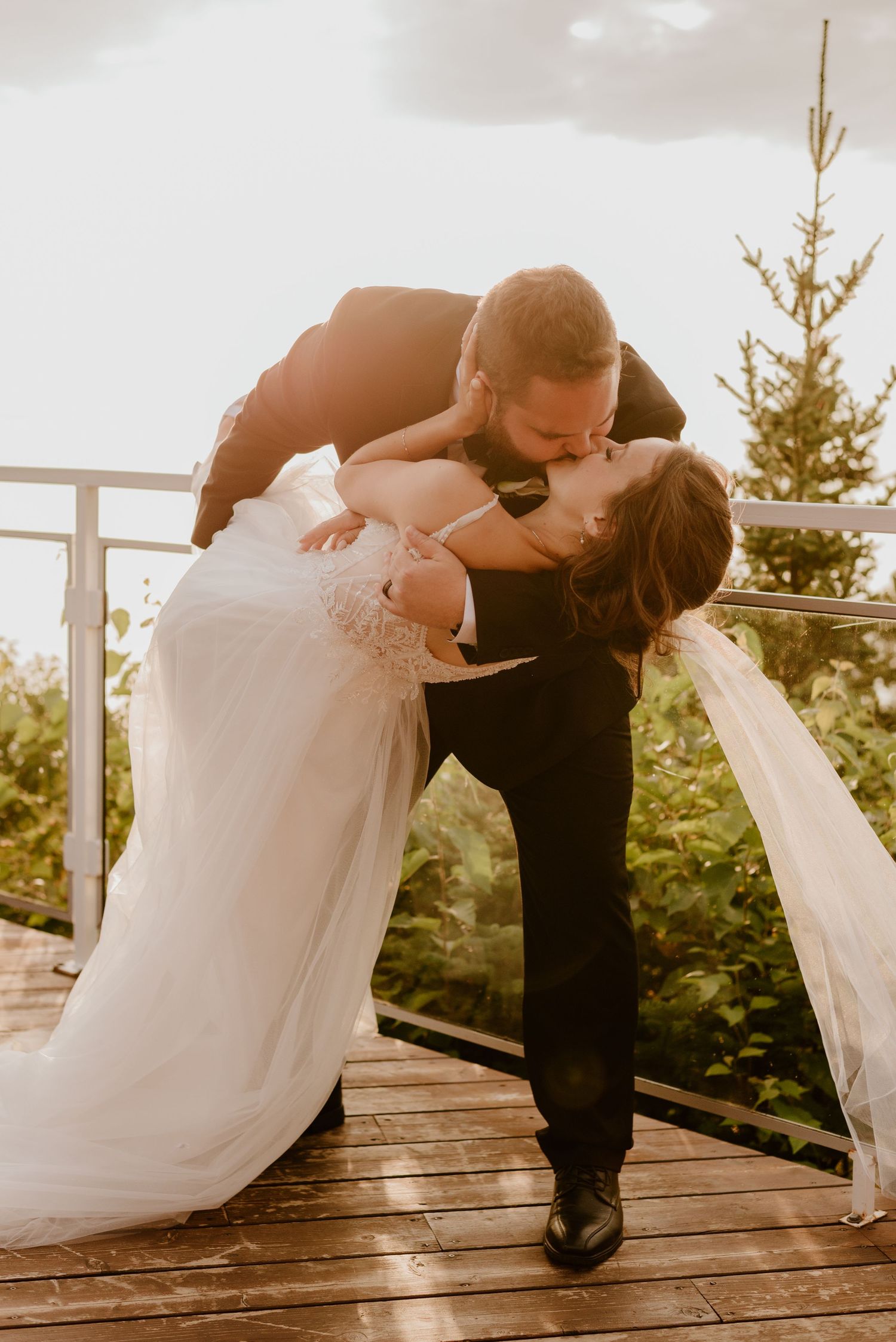 Romantic dip kiss on outdoor deck with scenic mountain backdrop and flowing white wedding dress.