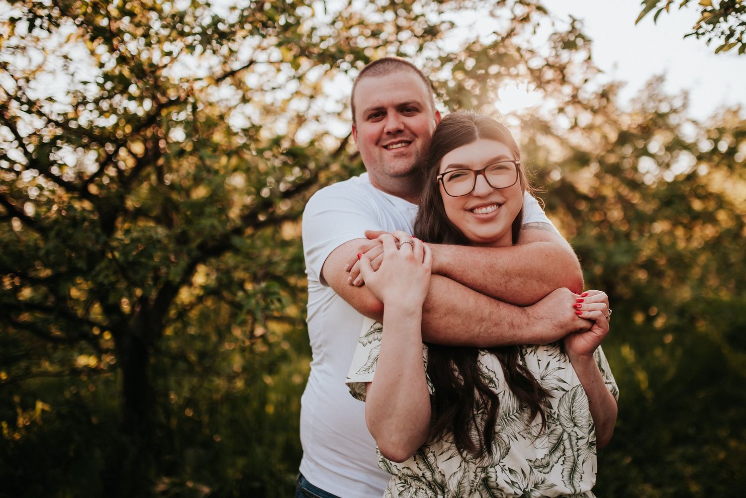 A joyful engagement photo of a couple embracing in golden sunset light.
