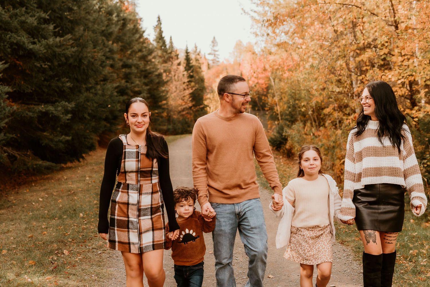 Family of five walking on a scenic autumn path surrounded by colorful fall foliage trees.