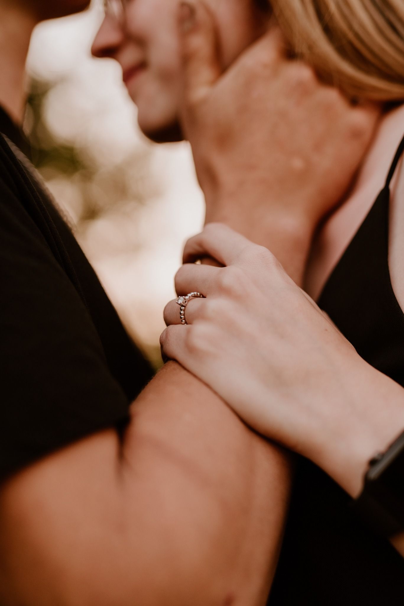Close-up shot of a delicate engagement ring on a hand against a warm blurred background.