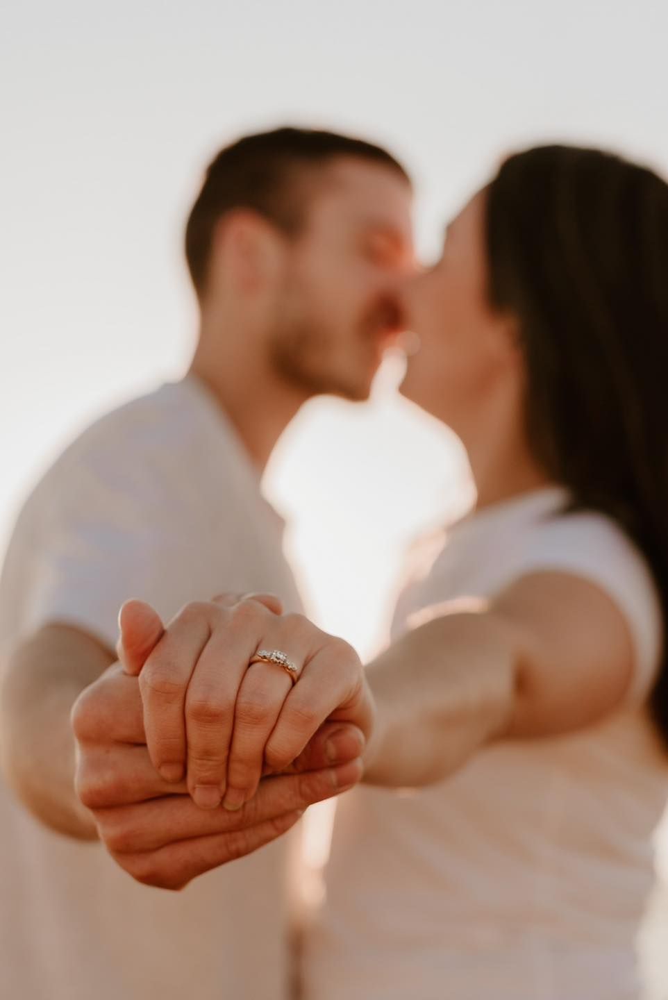 Closeup of hands with engagement ring touching as couple shares intimate moment during sunset.