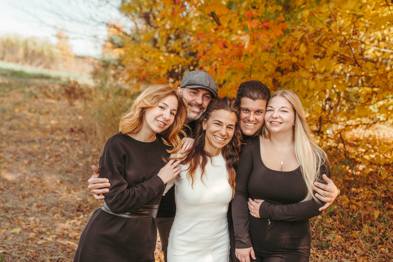 Group of five friends smiling together outdoors among vibrant autumn foliage in fall season photo.