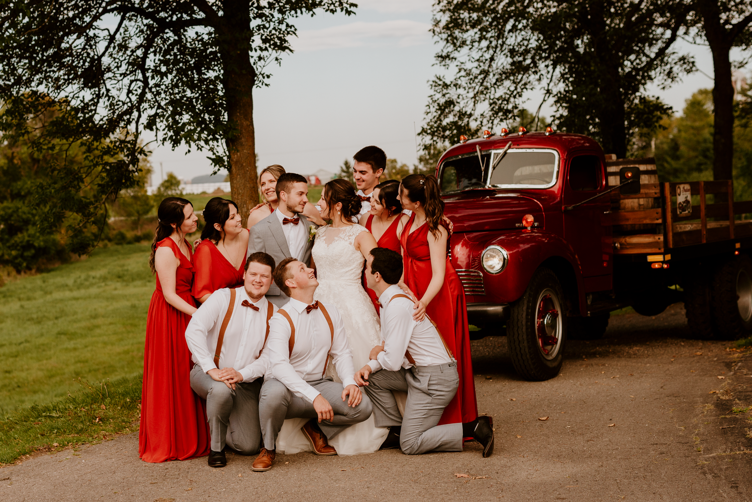 Moment authentique partagé entre des mariés et leurs invités d'honneur, devant un camion d'époque, sur une route de campagne rustique.
