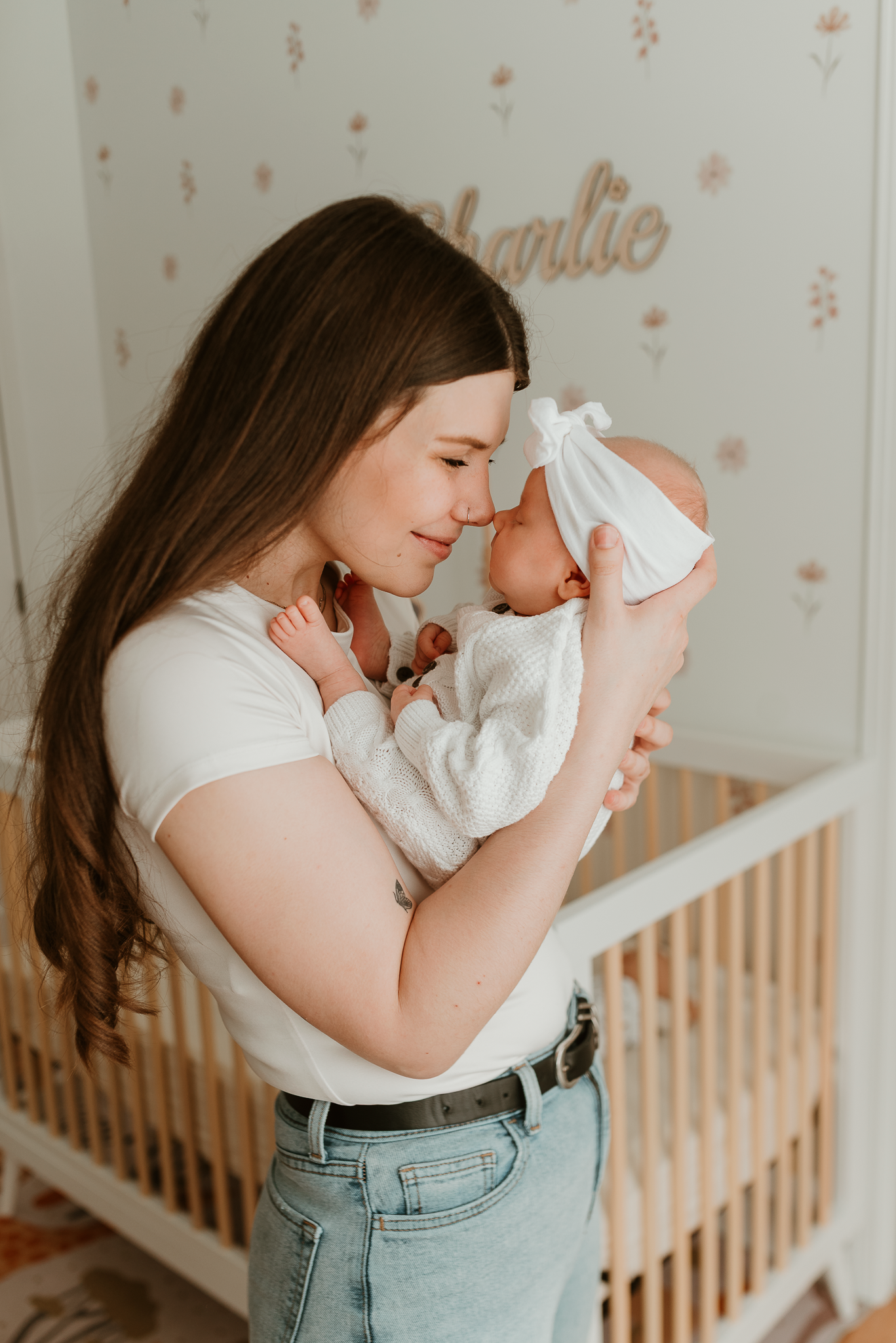A young mother tenderly touches foreheads with her newborn baby girl named Charlie in a decorated nursery.