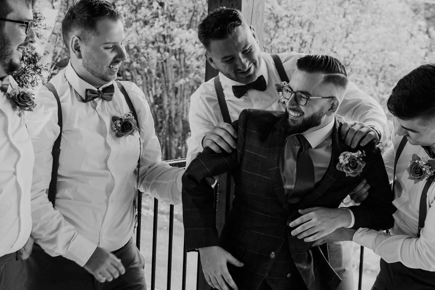 Black and white photo of groomsmen in bowties and suspenders sharing a drink together.