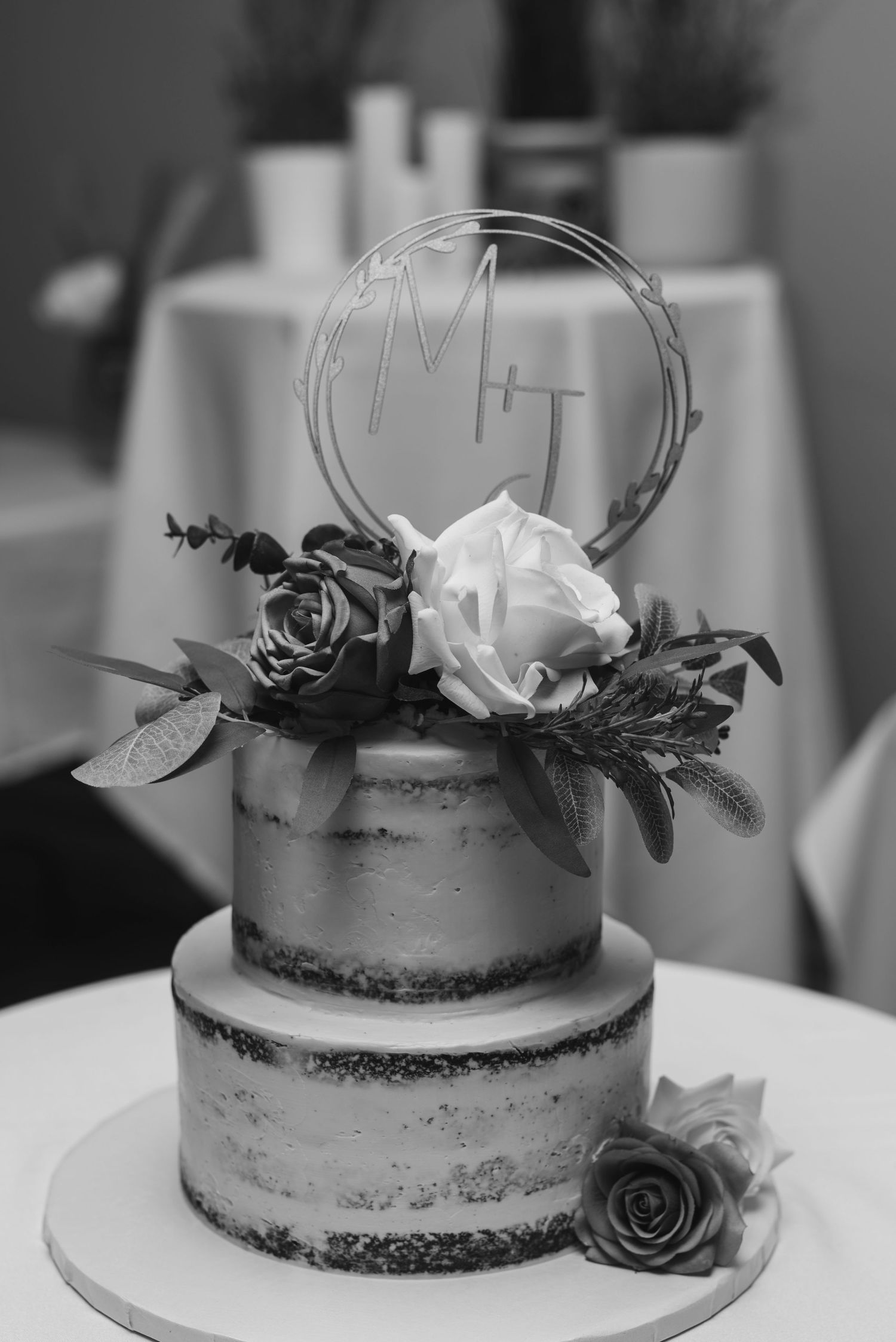 Elegant two-tier wedding cake decorated with roses and a circular topper.